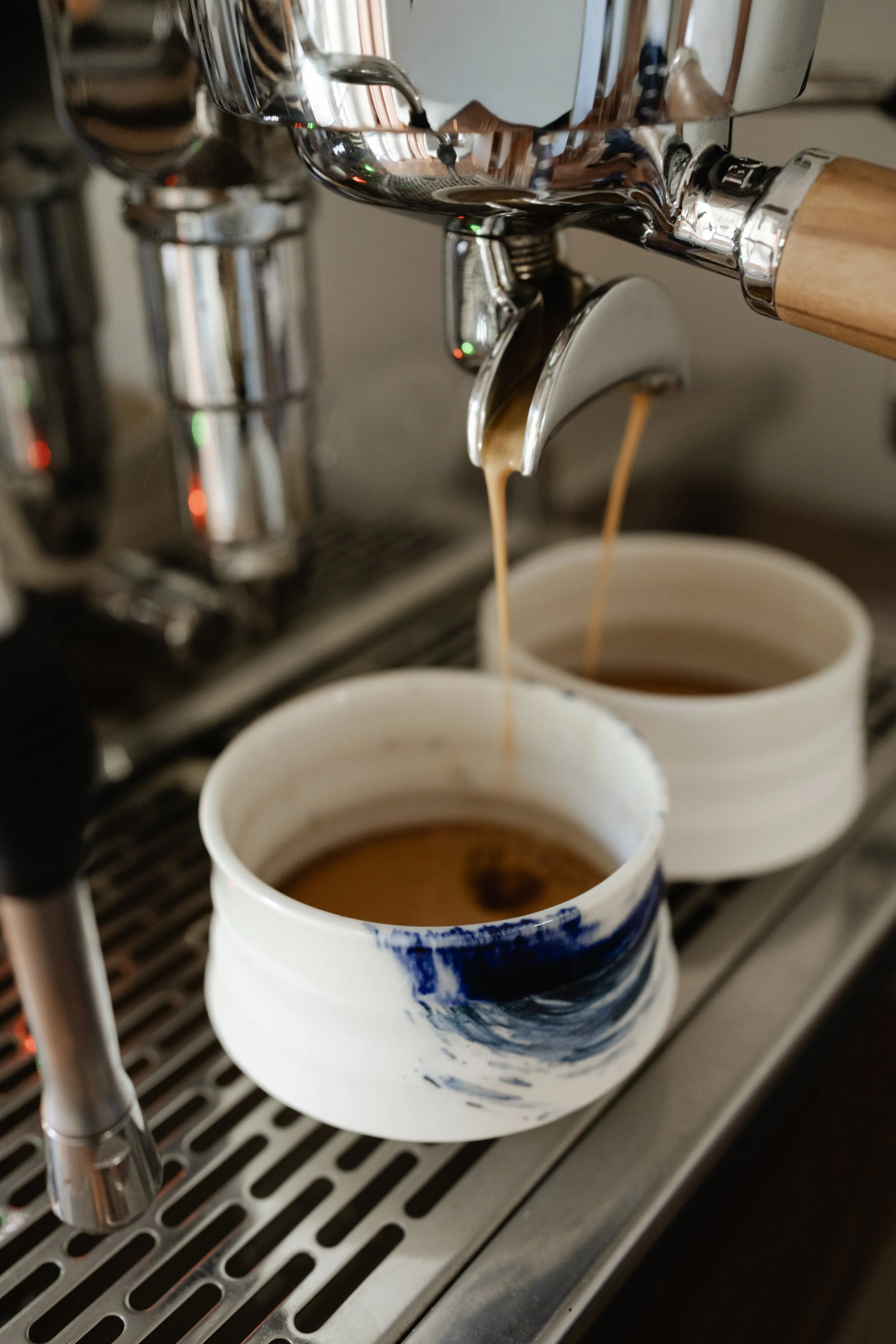Frischer Kaffee läuft aus Siebträgermaschine in zwei Porzellanbecher.