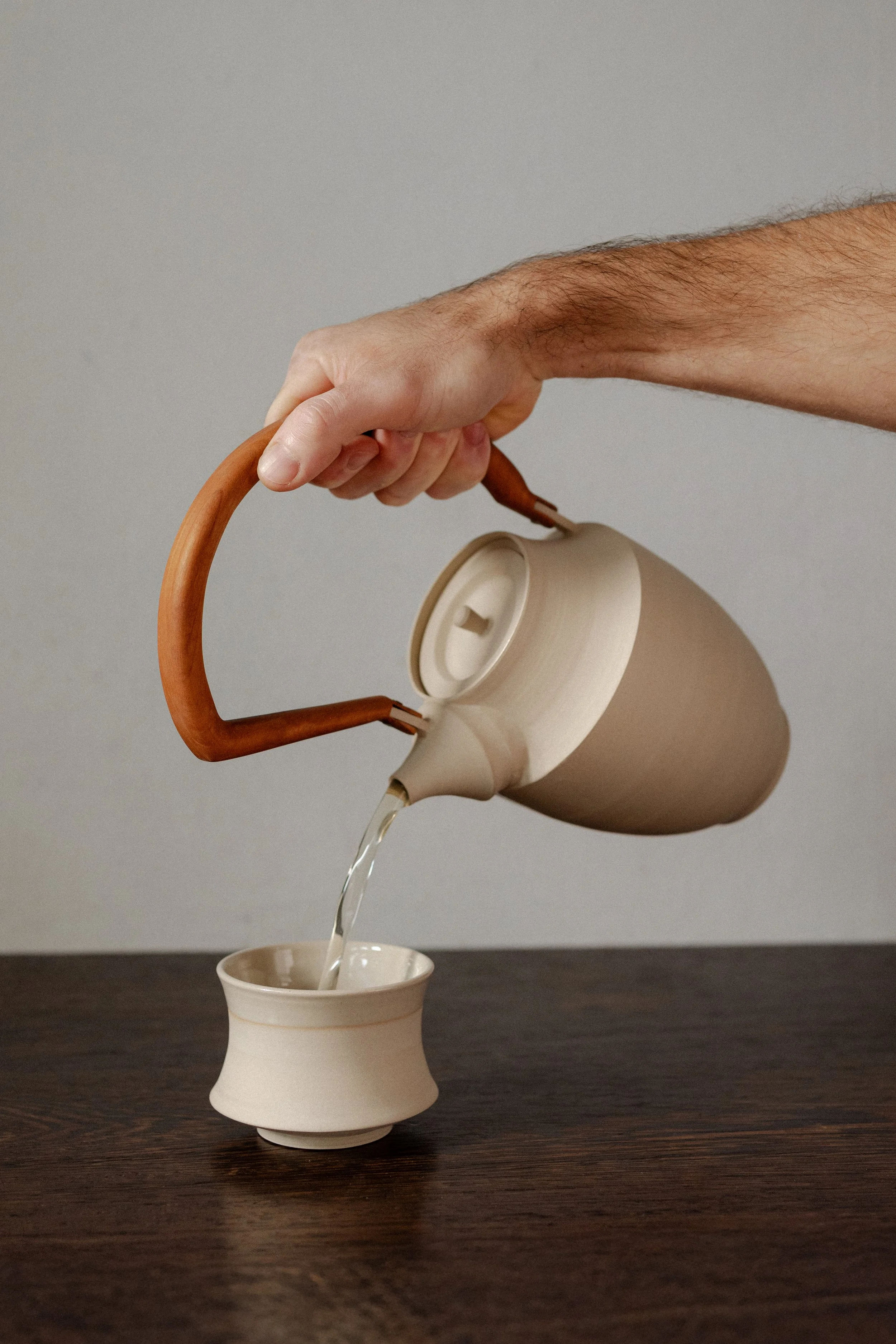 Hand giesst Tee mit Teekanne in einen Becher ein.