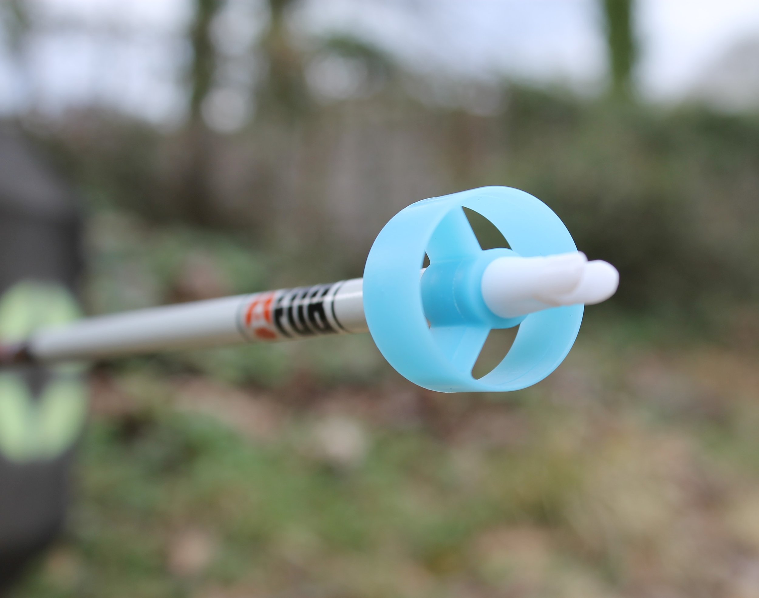 Close-up of a blue and white nasal spray bottle held outdoors with a blurred green and brown background.