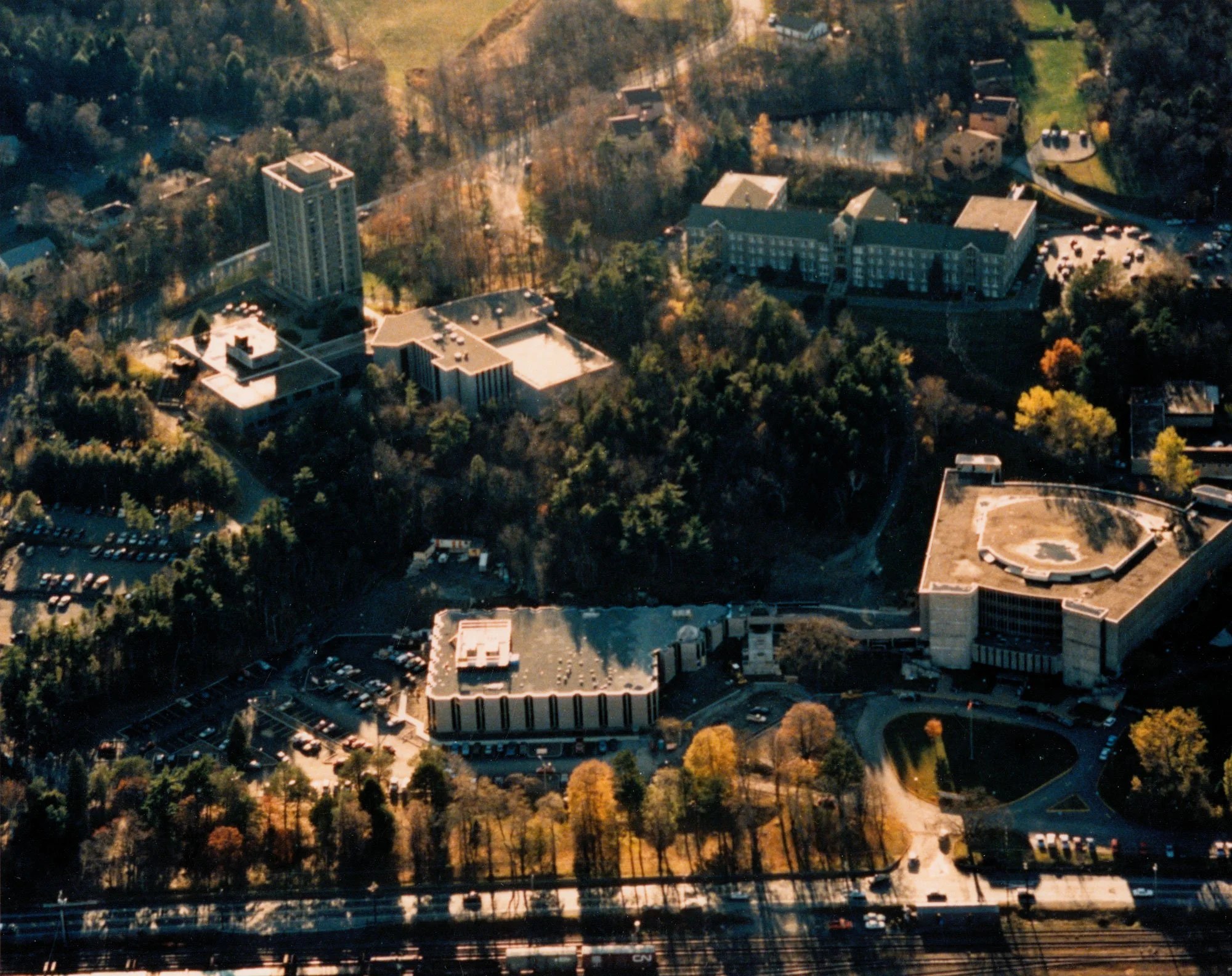 An aerial view of roof built by outcape in moncton with multiple buildings surrounded by trees, parking lots, and a nearby road with moving vehicles.