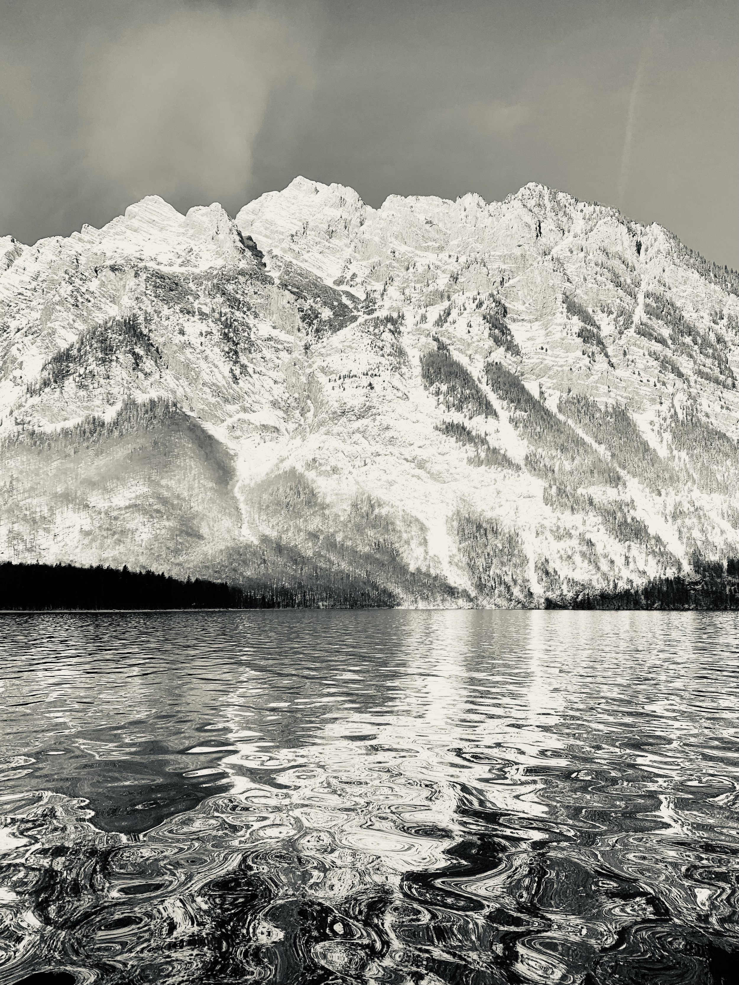 Gipfel eines verschneiten Berges über einem ruhigen See mit reflektiertem Bergpanorama in Schwarz-Weiß