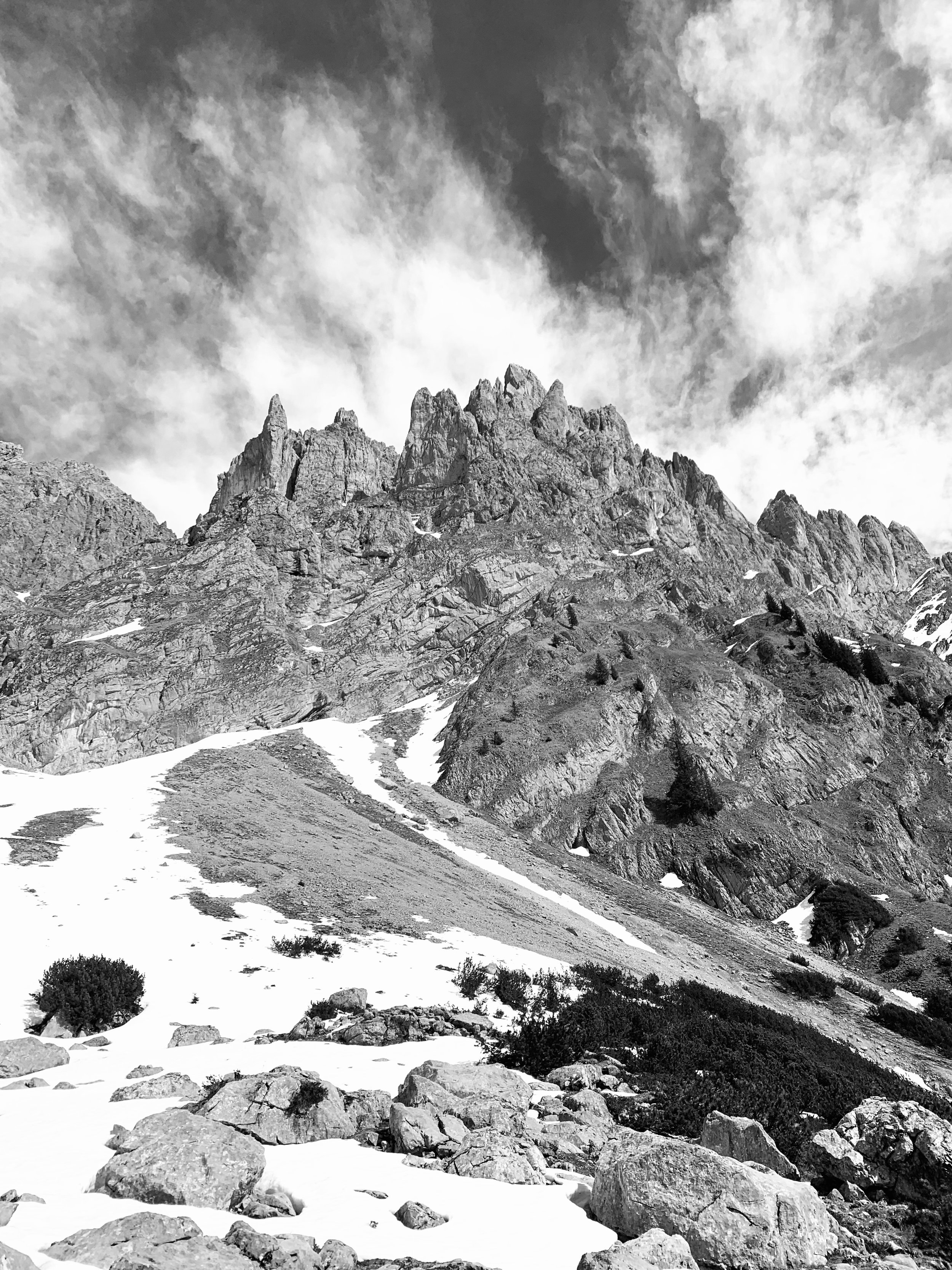Berglandschaft mit schneebedecktem Hang, Felsen und Wolken im Himmel, schwarz-weiße Aufnahme