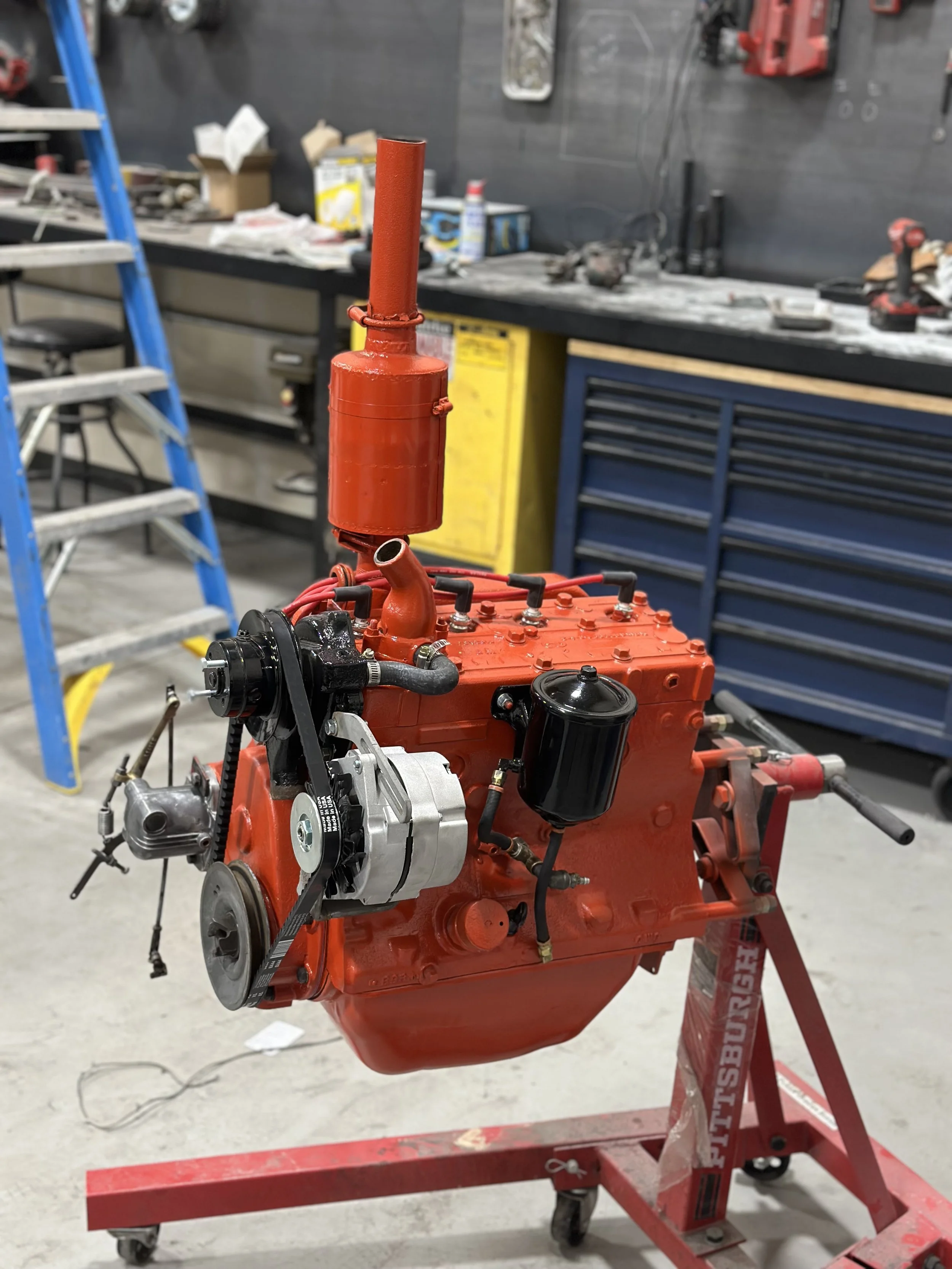 A vintage red engine mounted on a red engine stand in a garage or workshop.