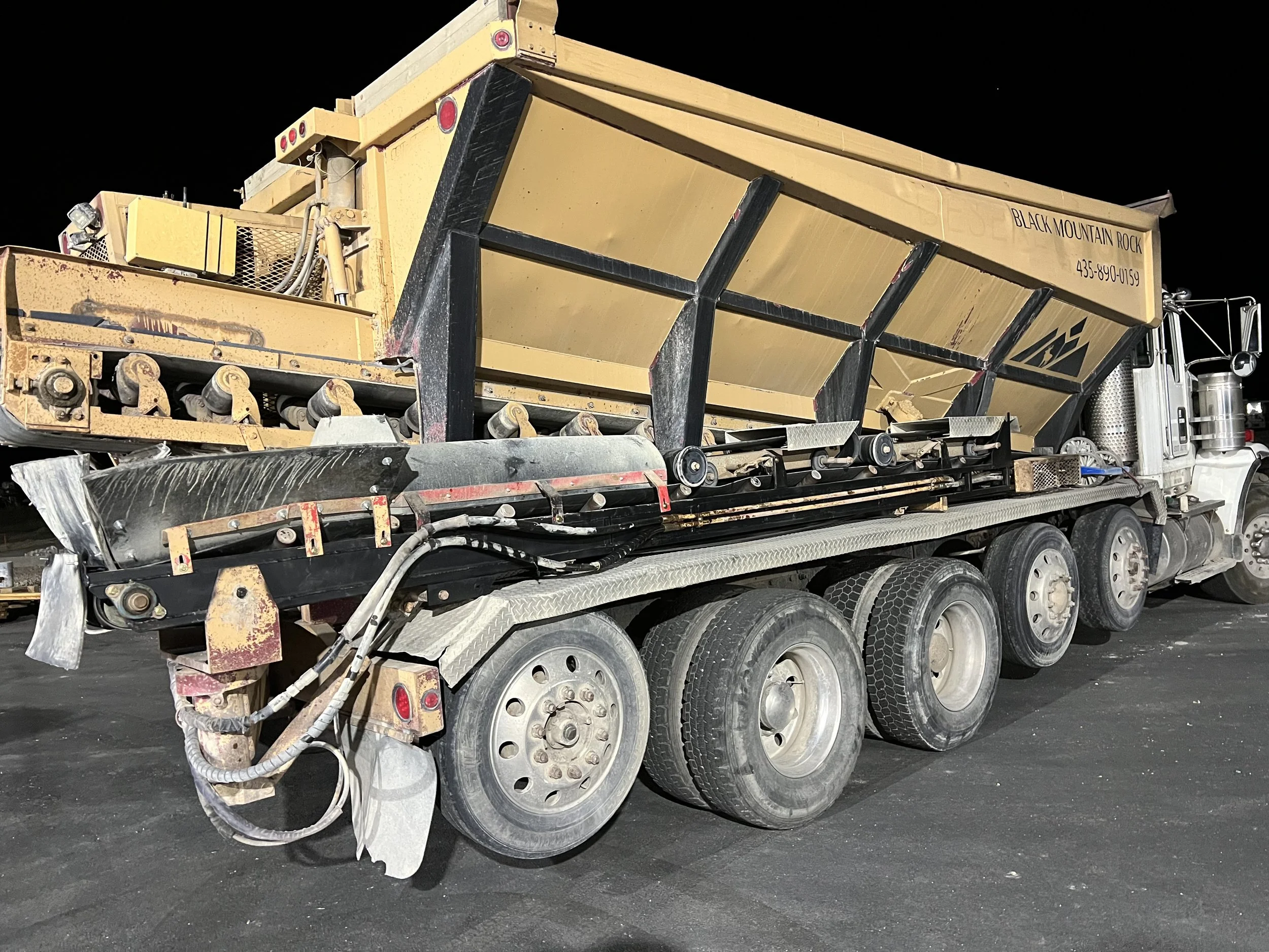 A large yellow dump truck with multiple wheels parked on an asphalt surface at night