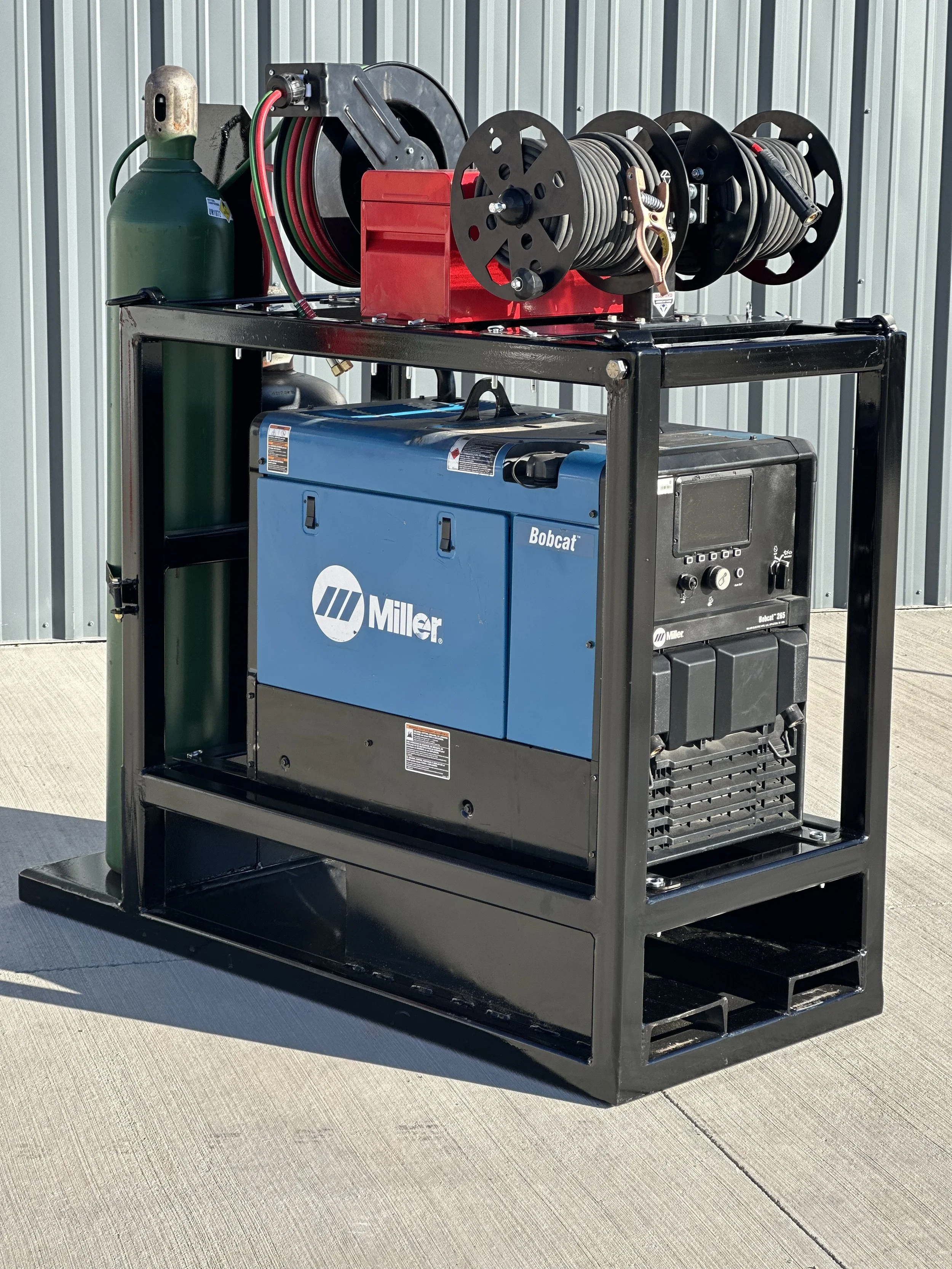 Portable industrial generator with hoses and a fire extinguisher, outdoors on concrete.
