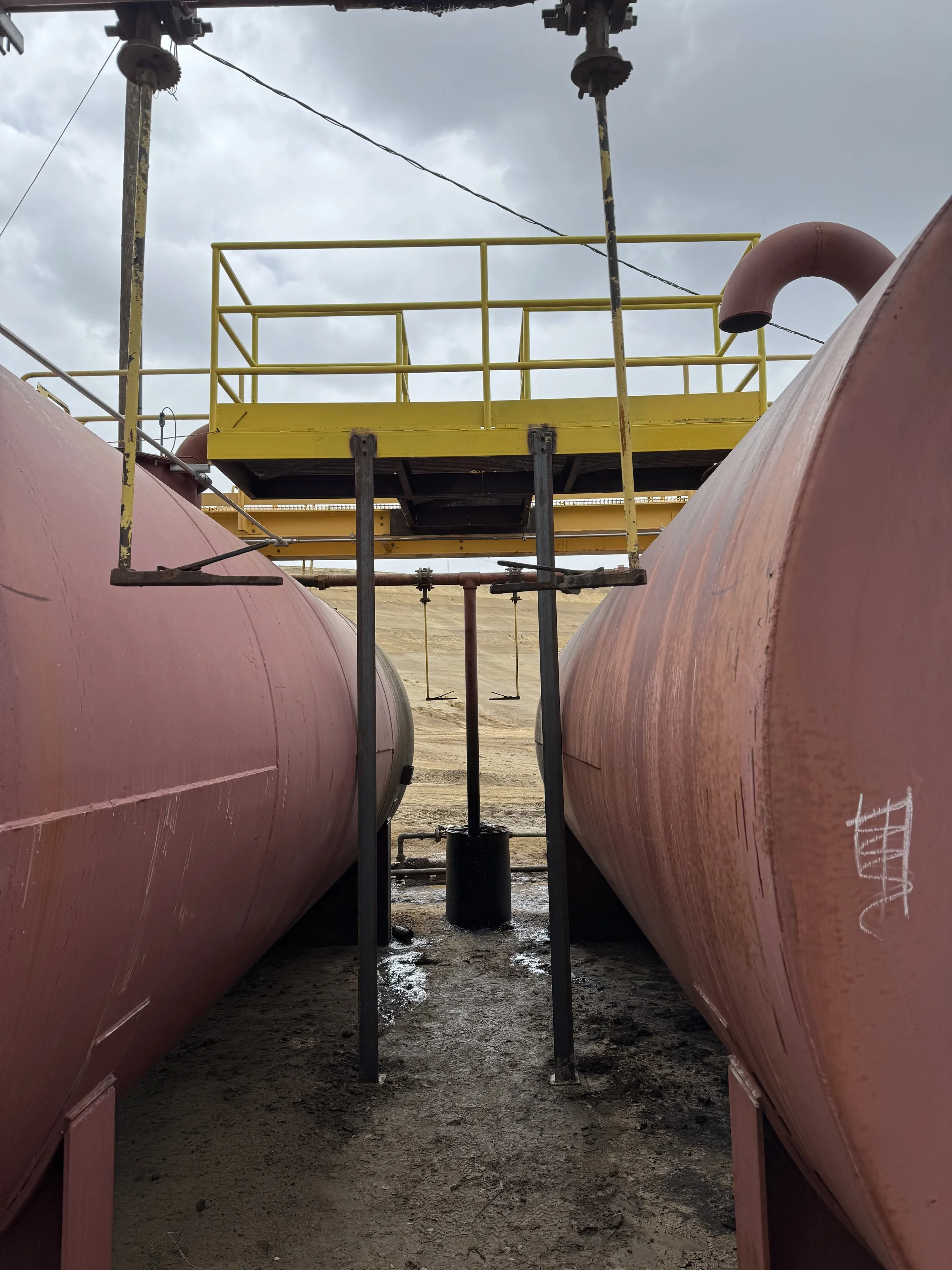 Industrial storage tanks with a yellow platform and railing, seen from below against a cloudy sky.