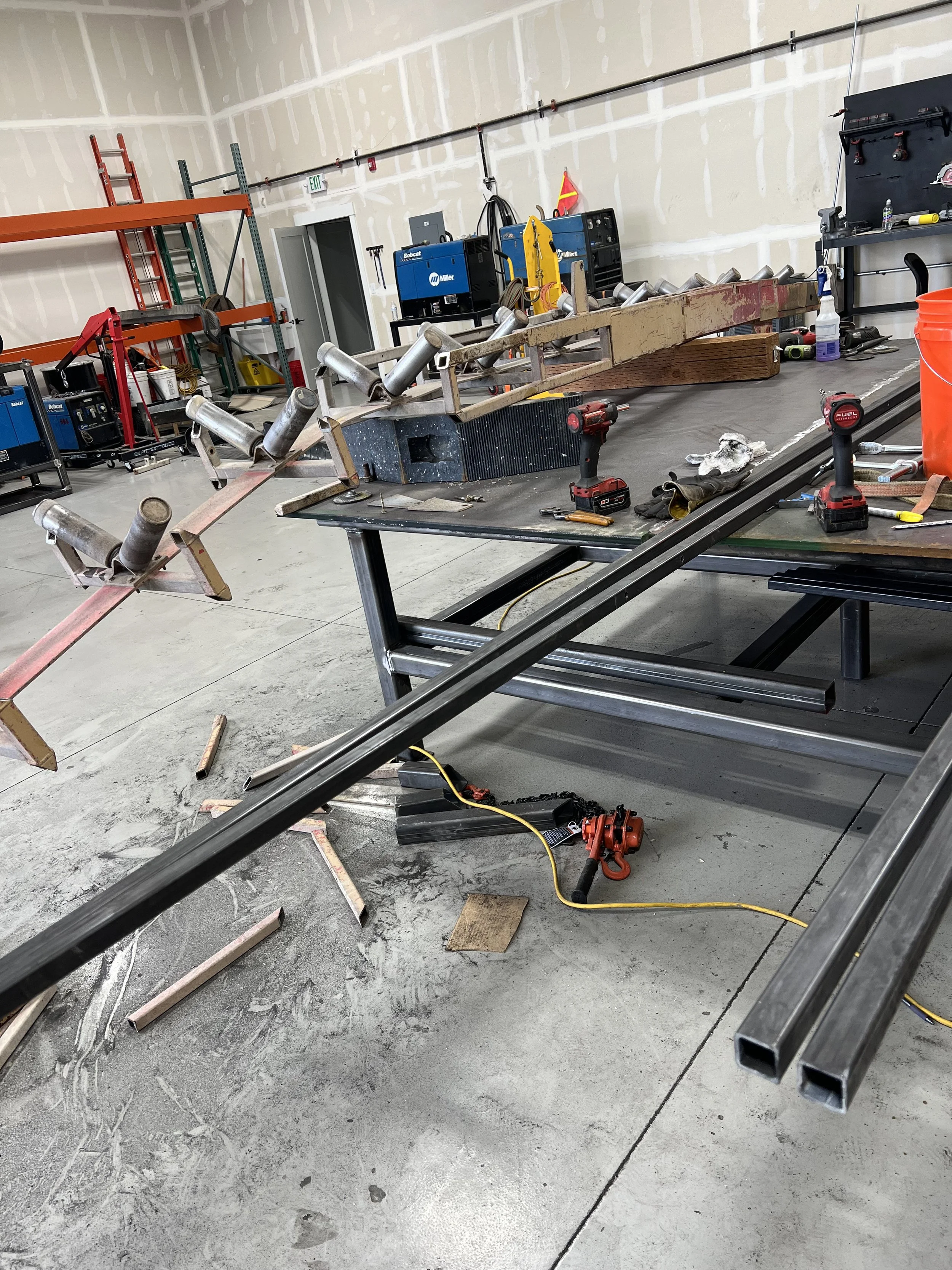 Workshop with metal pipes, tools, and workbenches in a construction or fabrication setting.