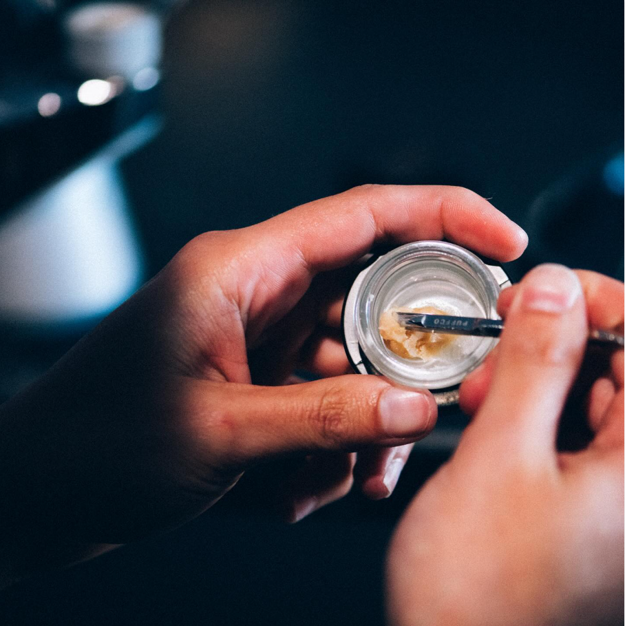 A person working on a small, round container with a jeweler's tool, possibly fixing or examining a piece of jewelry or watch part.