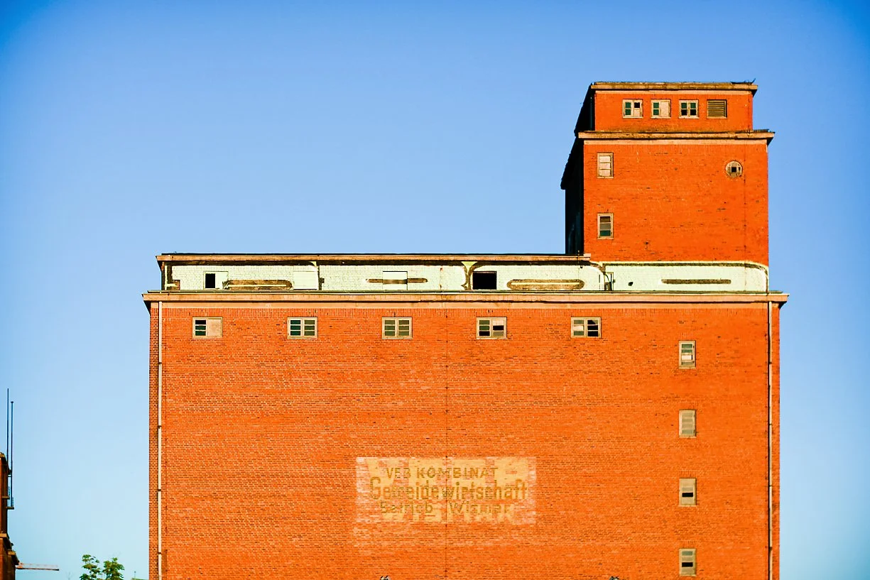 A tall red brick industrial building with a blue sky background.
