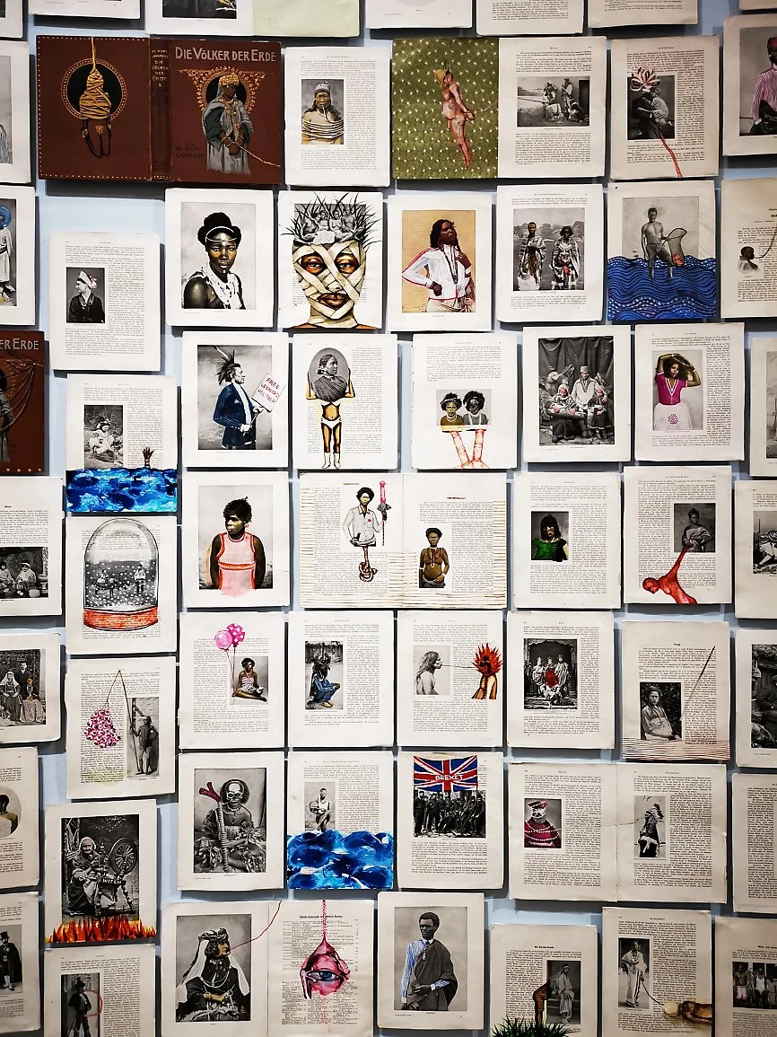 En vegg med mange aviser eller magasinark med fotografier av afrikanske mennesker, noen med ansiktsmalerier, og fargerike bilder og illustrasjoner.