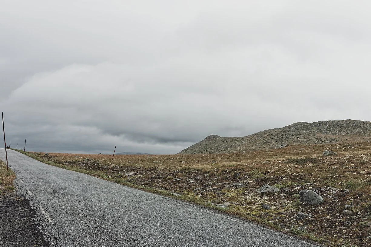 En ensartet landevei som går gjennom et flatt, tørt landskap med lave åser i bakgrunnen under en overskyet himmel.