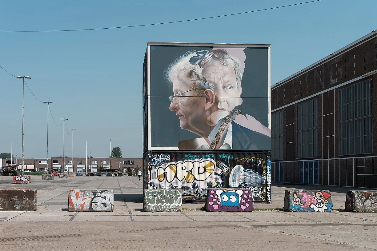 En stor vegg med graffiti og en stor plakat av to personer som er sammenfiltret, en eldre kvinne og en eldre mann i en kunstnerisk sammenstilling.