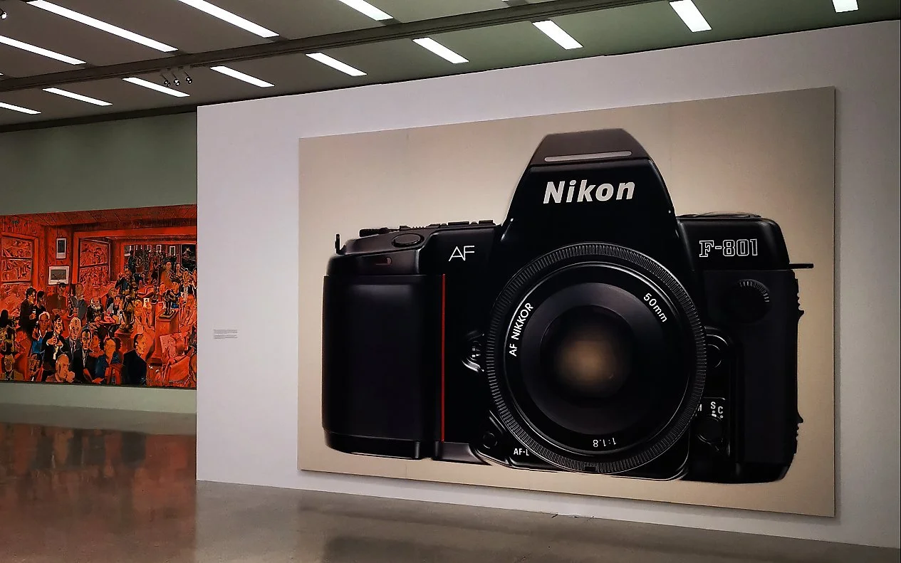 Stor kunstutstilling med et stort bilde av en Nikon F-801 kamera på veggen