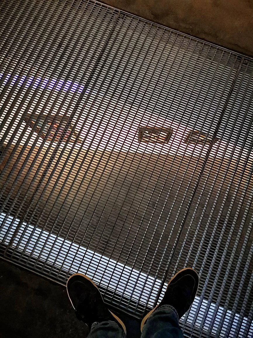 Følger en person i sneakers og jeans en metallristet gulv i et industri- eller bygningmiljø.
