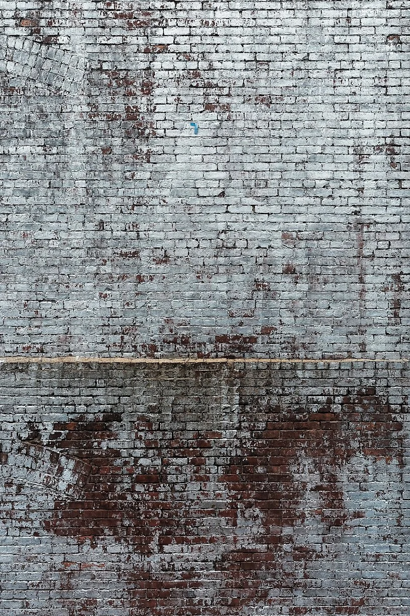 Old brick wall with peeling paint, stains, and a faint outline of a painted or faded advertisement.