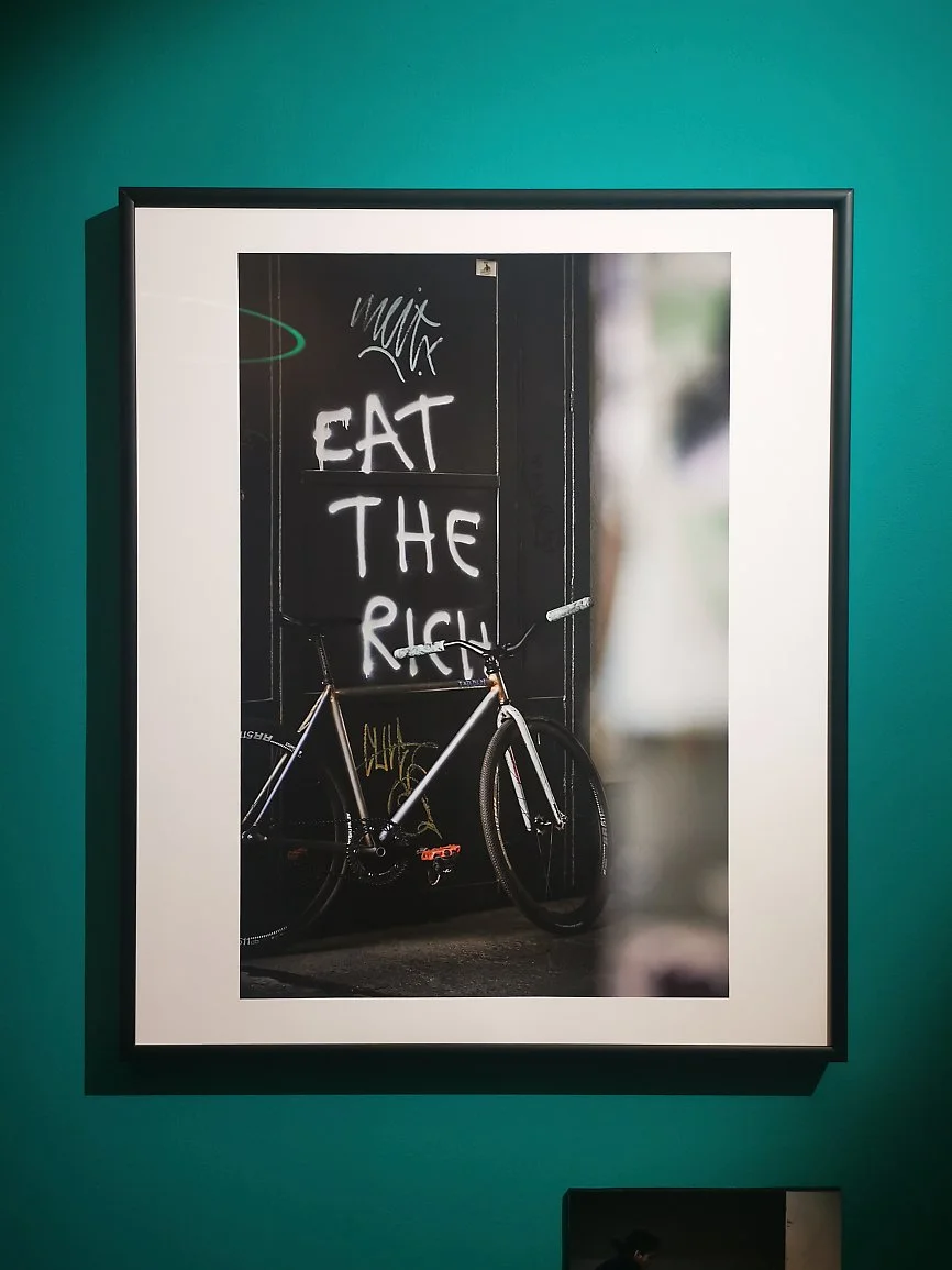 Fotografi av en vegg med graffiti som sier 'EAT THE RICH' og en sykkel foran