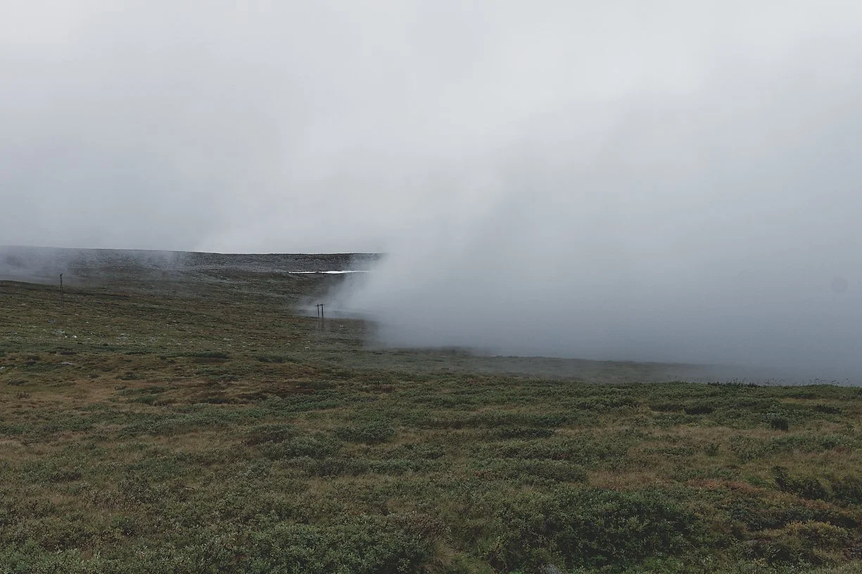 Et fjellandskap med tåke eller skodde som ruller inn over det grønne landskapet.