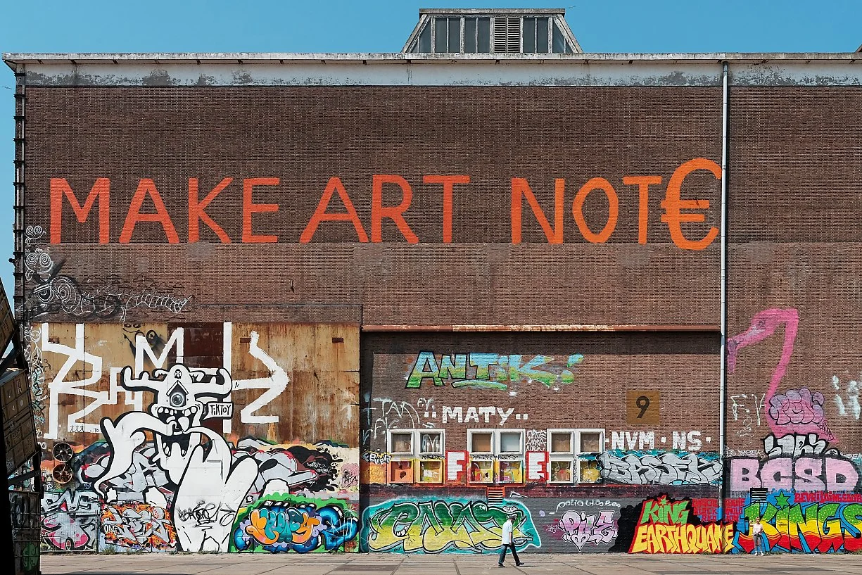 Graffiti på en mur med teksten «MAKE ART NOT» og en stor EU-flaggbue