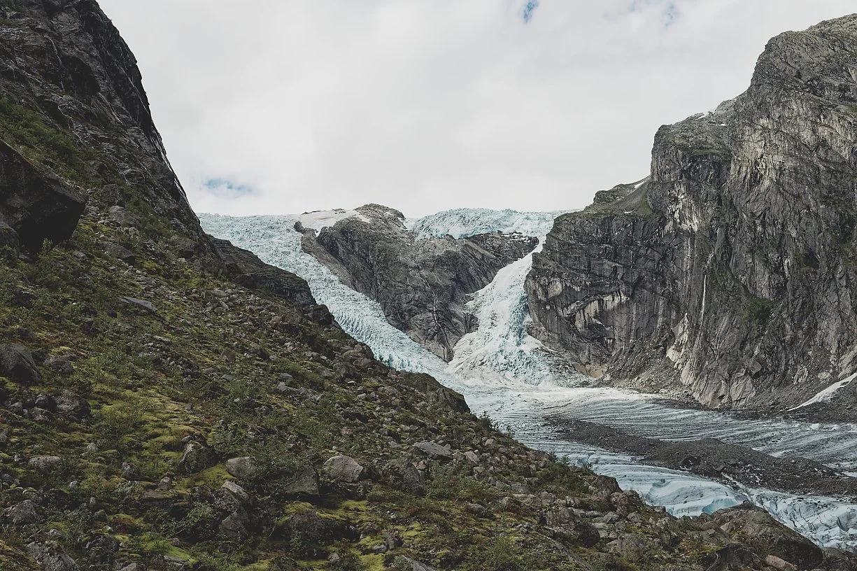 Et fjellandskap med snø- og isbreer, bratte fjellvegger og en skogkledd skråning.