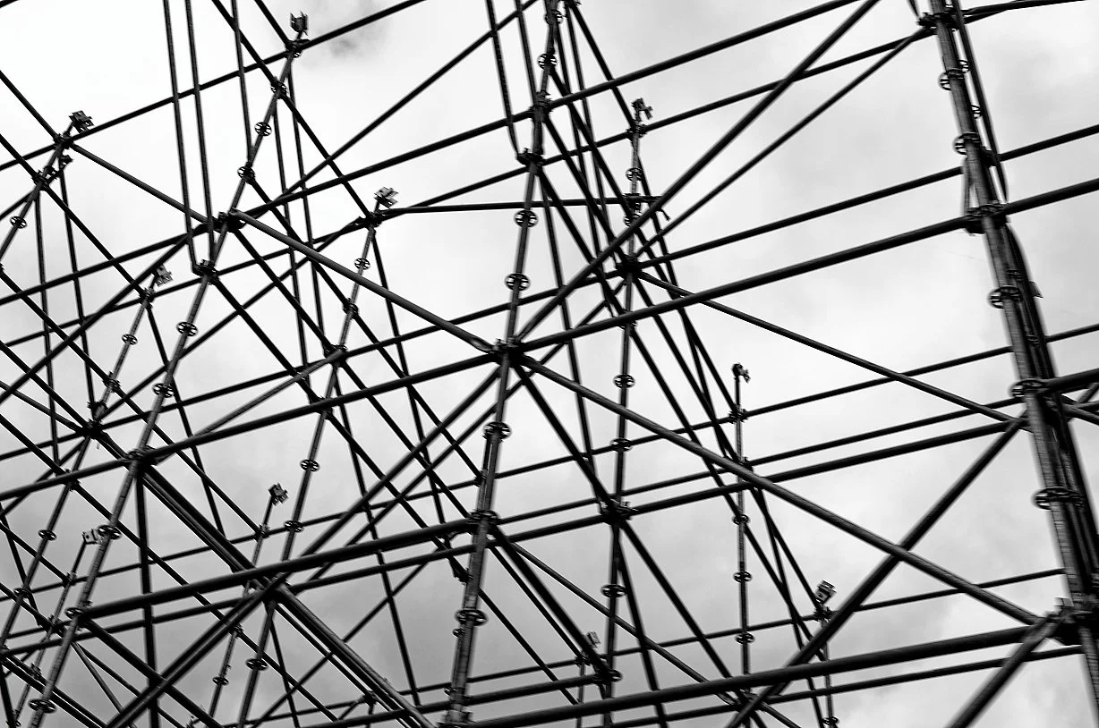 Black and white photo of a complex network of metal scaffolding against a cloudy sky.