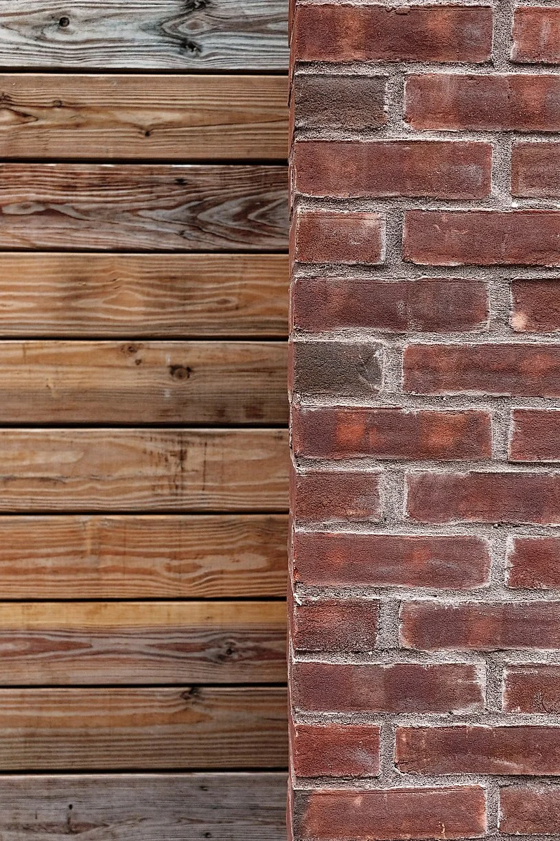 Close-up of a brick wall on the right side and a wooden fence or wall on the left side.