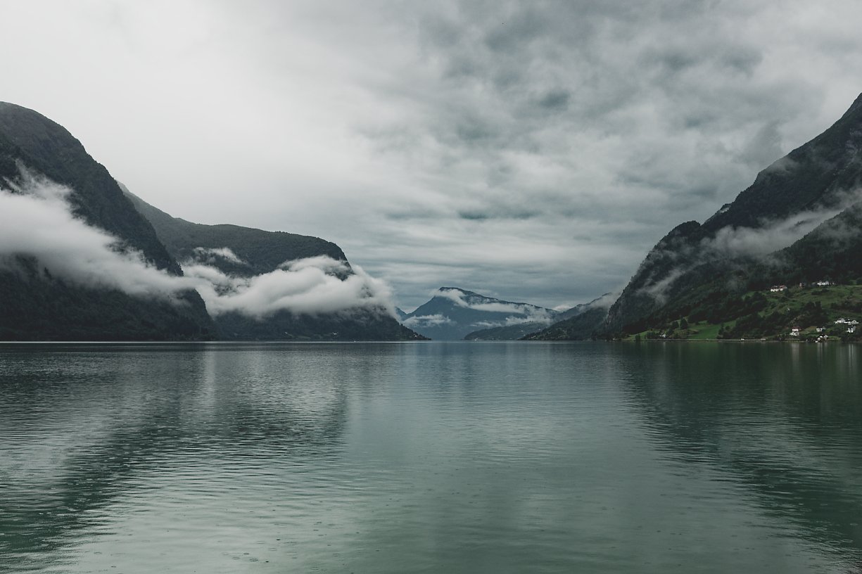 Fjord med fjell, vann og skyer.