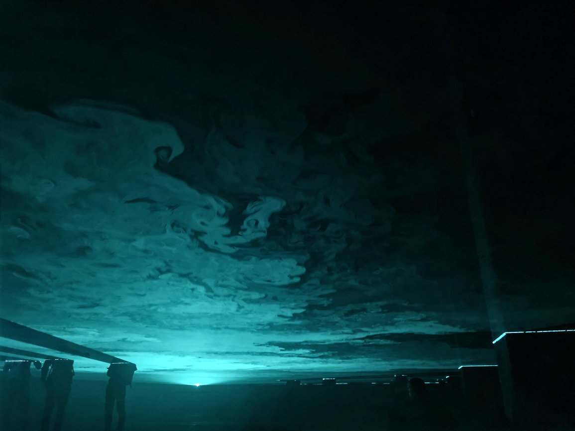 Mennesker som ser på en digital kunstinstallasjon med blå lys og skiftende mønstre på taket.