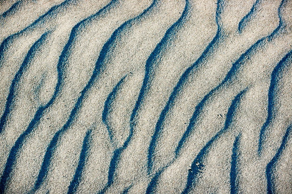 Close-up of sand with blue lines forming wave patterns in the sand.