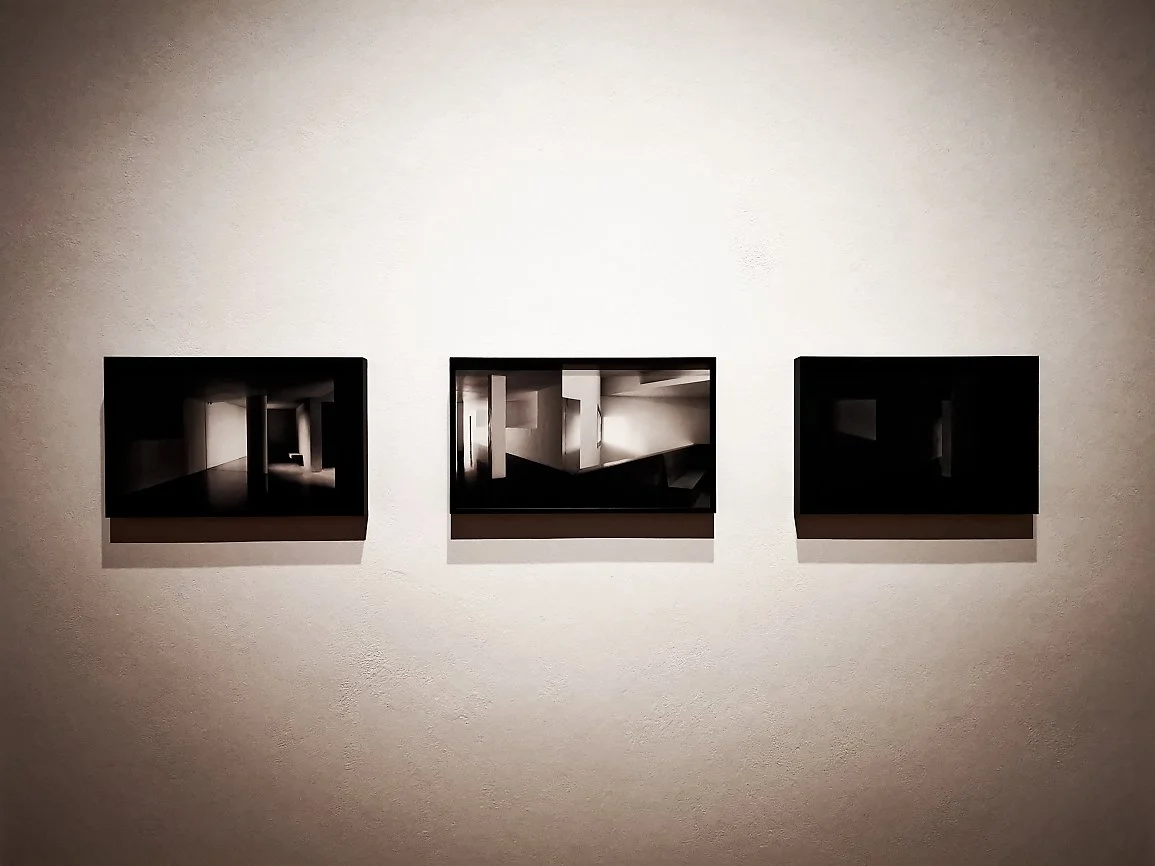 Tre fotografier av kunstverk eller installasjoner på en vegg i en kunstutstilling, med skygger og refleksjoner.