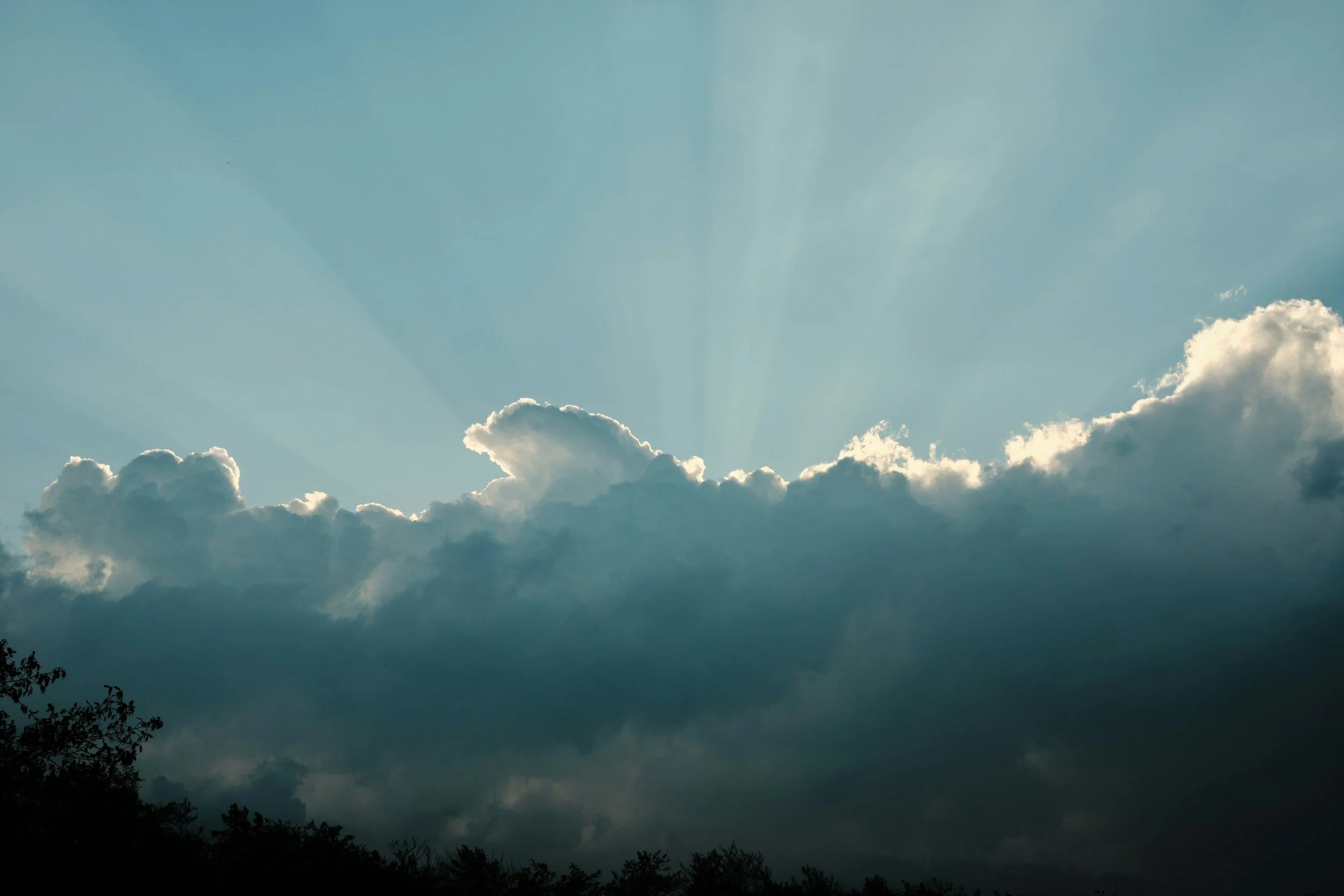Cloudy sky with the sun behind the clouds and rays of sunlight shining through.