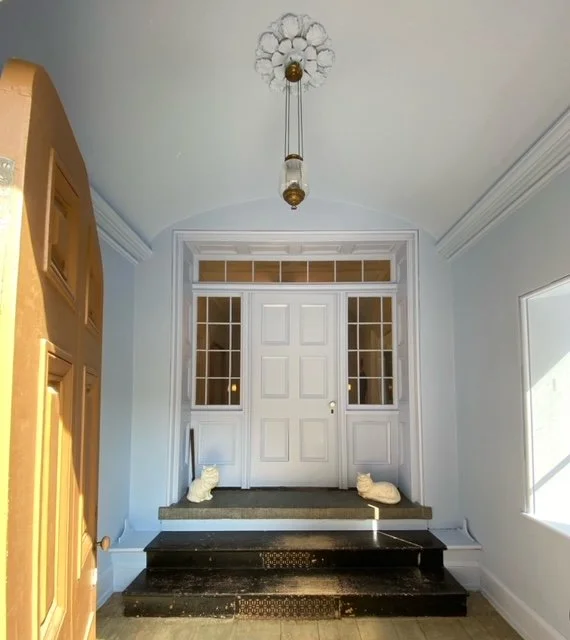 Entryway with a white door and glass panels, black steps, and two ceramic cat figurines sitting on the steps.