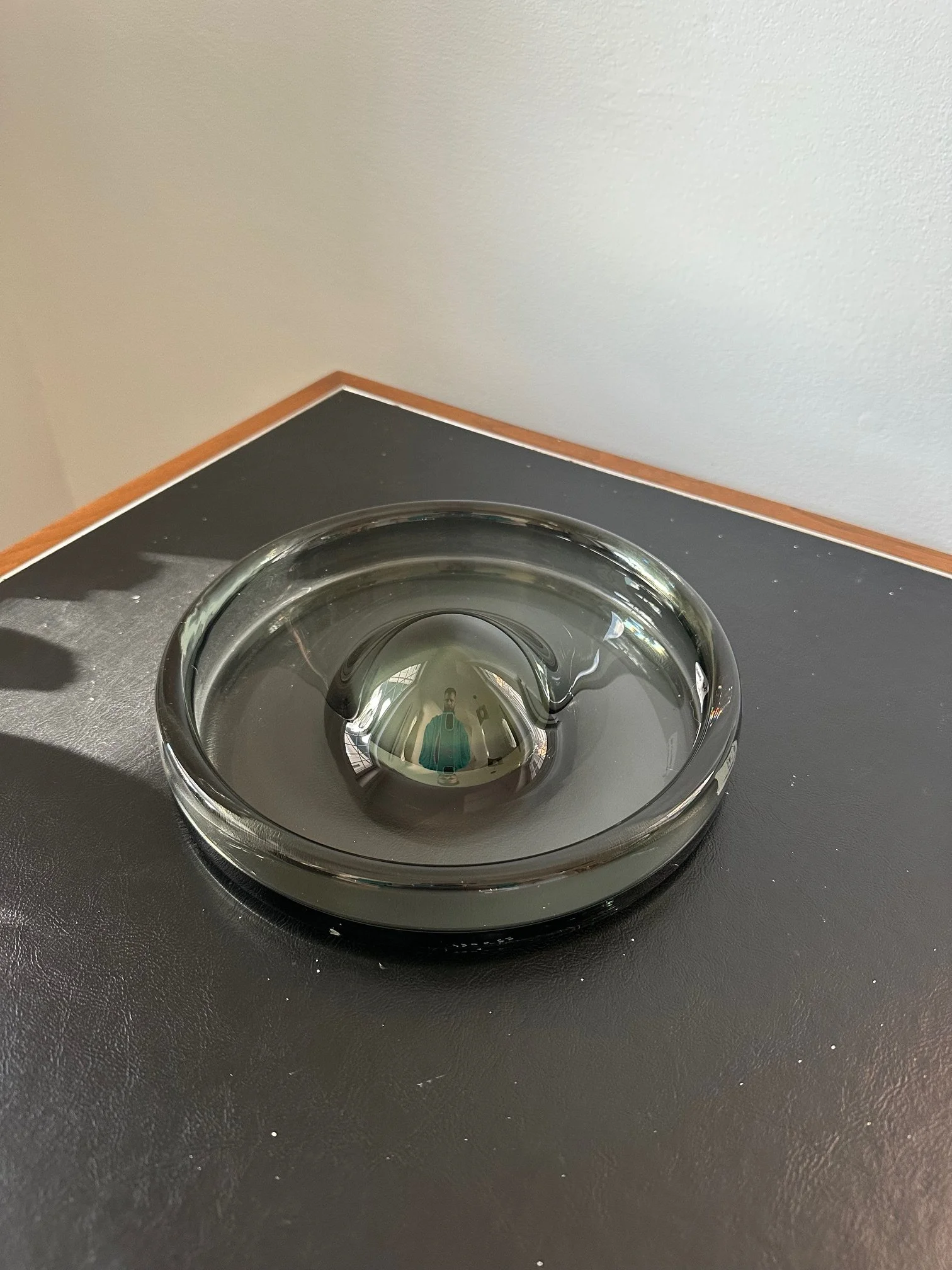 A glass bowl filled with clear water placed on a black countertop with some white specks, against a white wall with a brown border at the top.