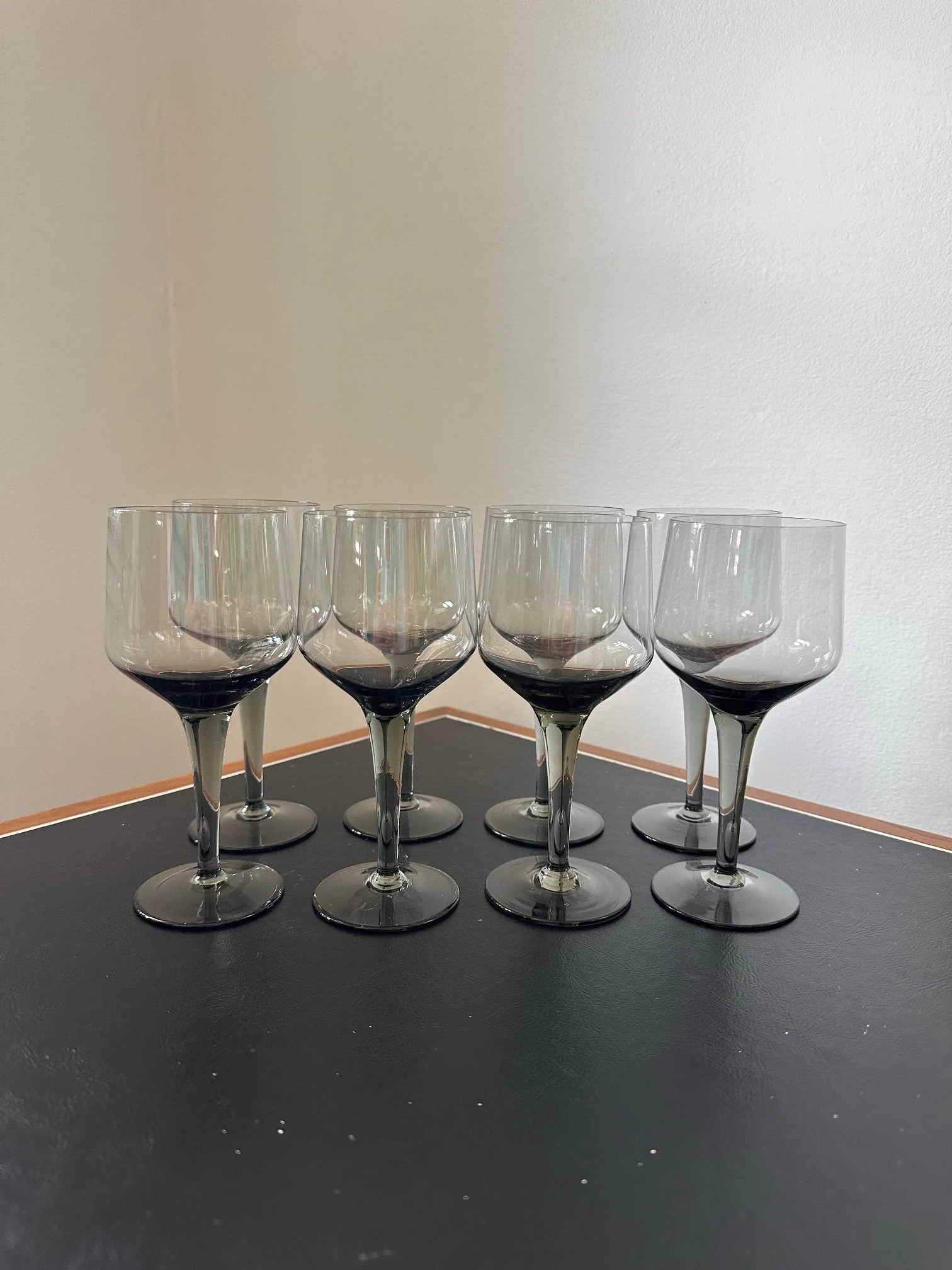 Eight empty wine glasses arranged in two rows on a black surface against a beige and white wall.