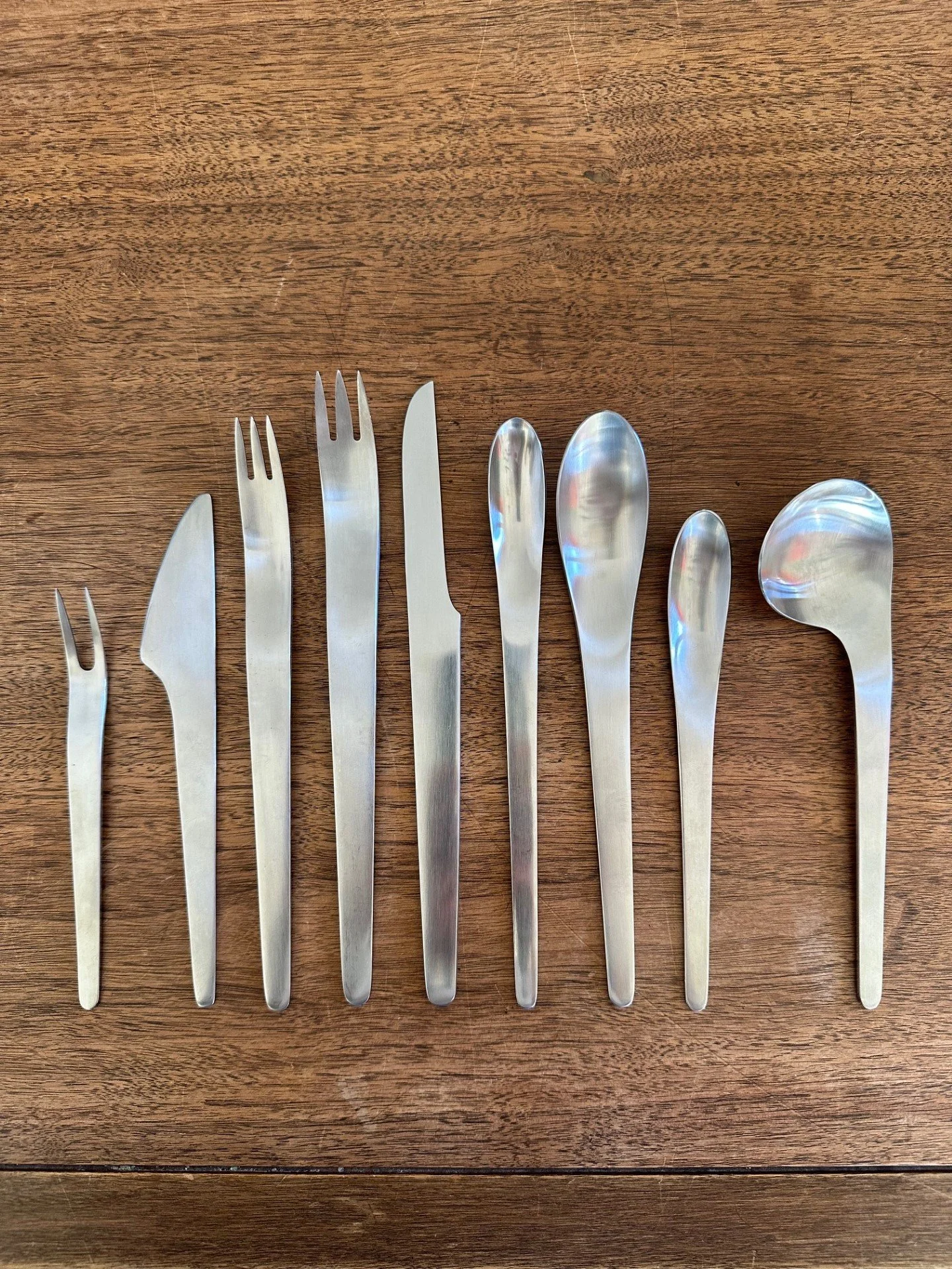 Set of eleven metal cutlery pieces including forks, knives, and spoons arranged on a wooden surface.