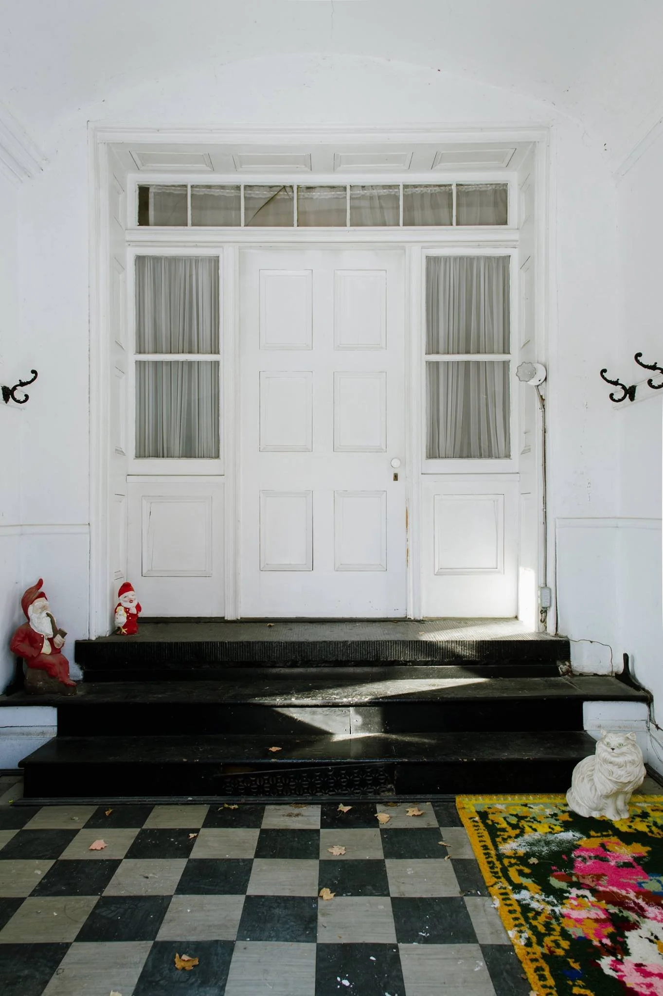 White door with window panels, black steps, holiday decorations including Santa statues, a white tiger figure, and a colorful rug in front.