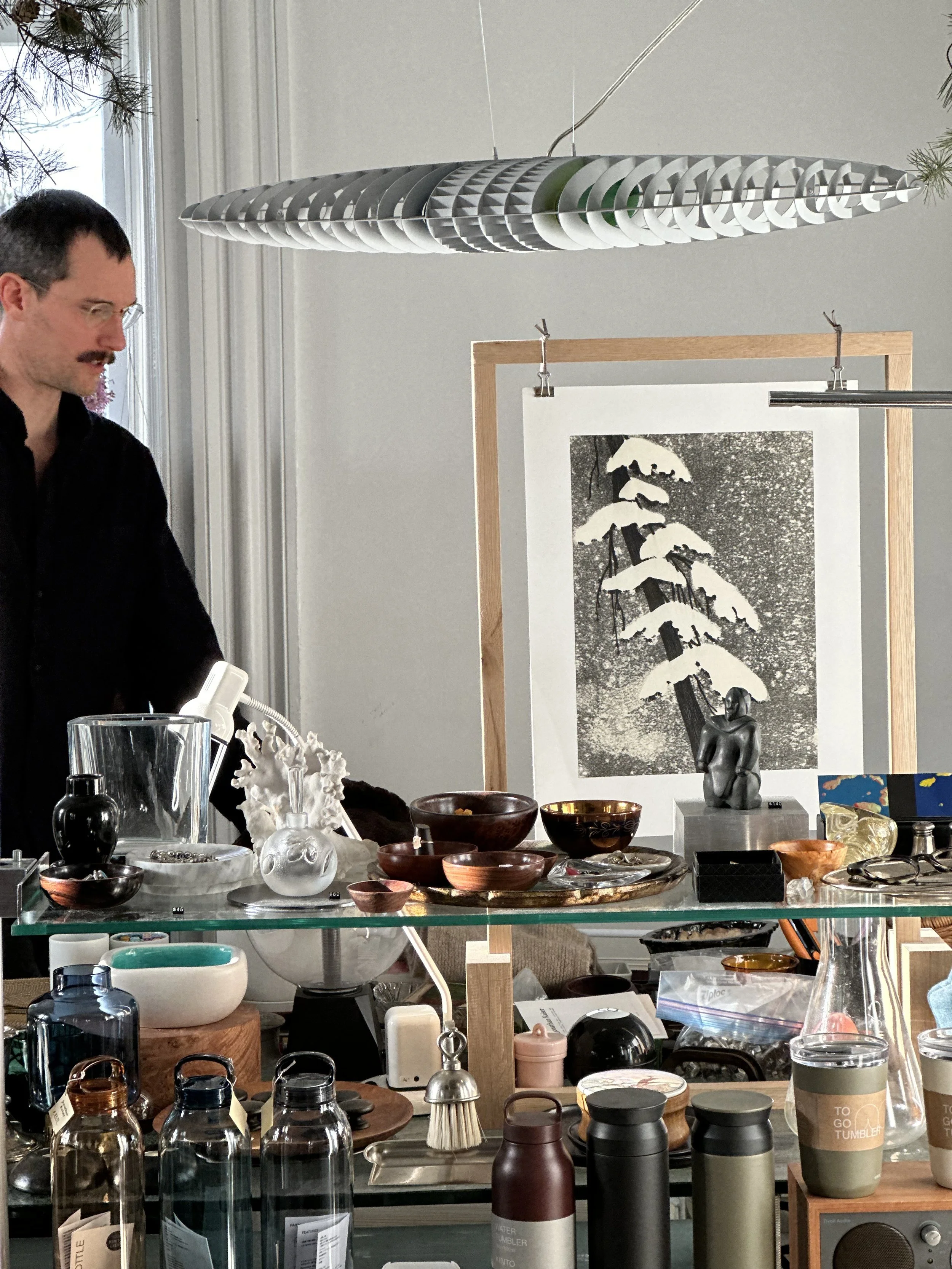 Various decorative and functional items on display at a market or shop, including bowls, bottles, cups, sculptures, and artwork.