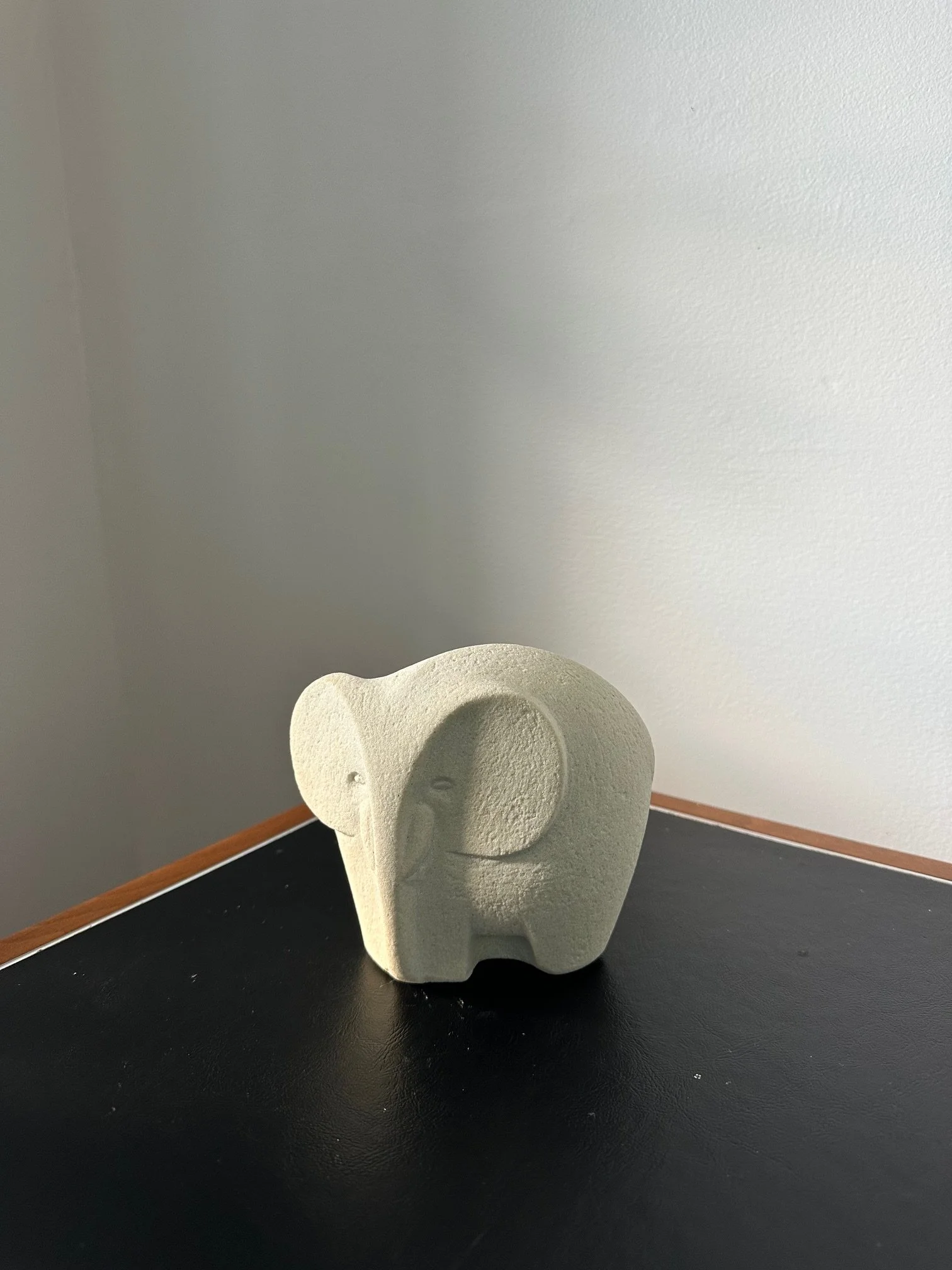 A beige elephant-shaped sculpture on a black table against a wall with a wooden baseboard.