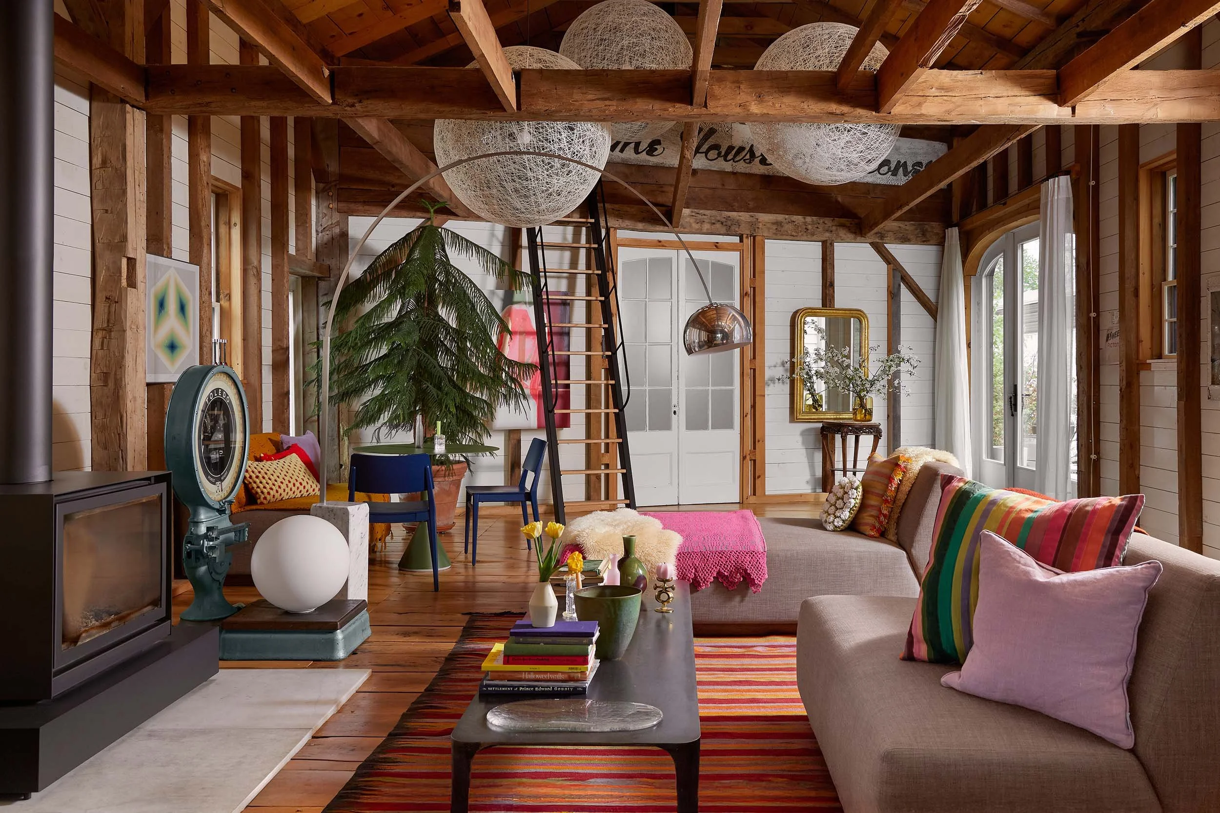 Living room with wooden beams, white walls, and eclectic furniture including colorful pillows, a sofa, and various decor items like lamps, vases, and a mirror.