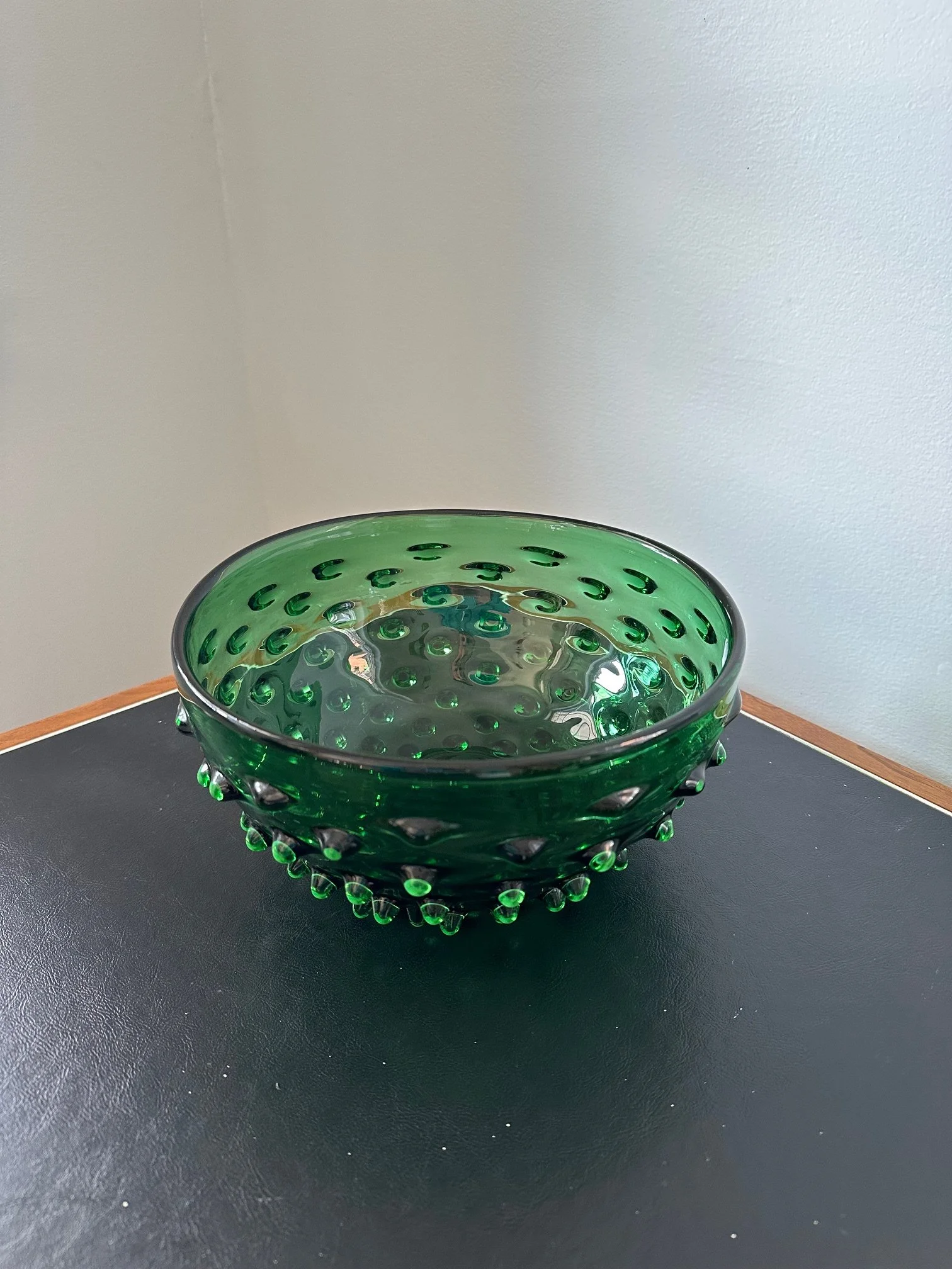 A green glass bowl with a dotted pattern sits on a black surface against a plain light-colored wall.