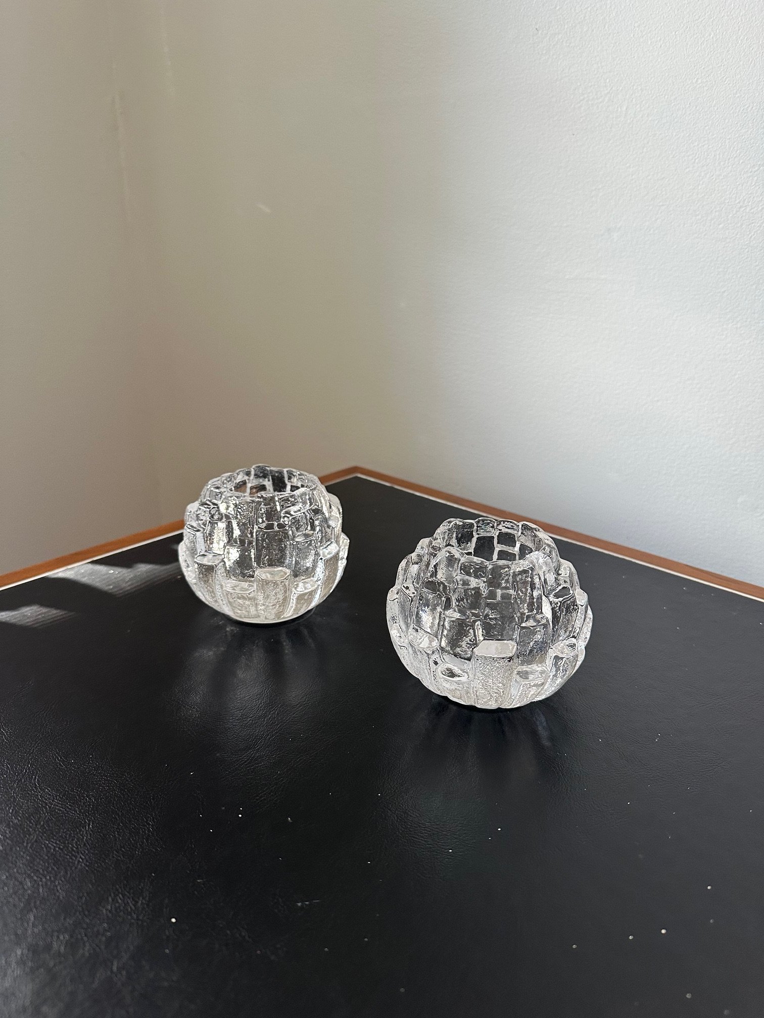 Three clear glass candle holders with a honeycomb pattern on a black surface against a plain white wall.