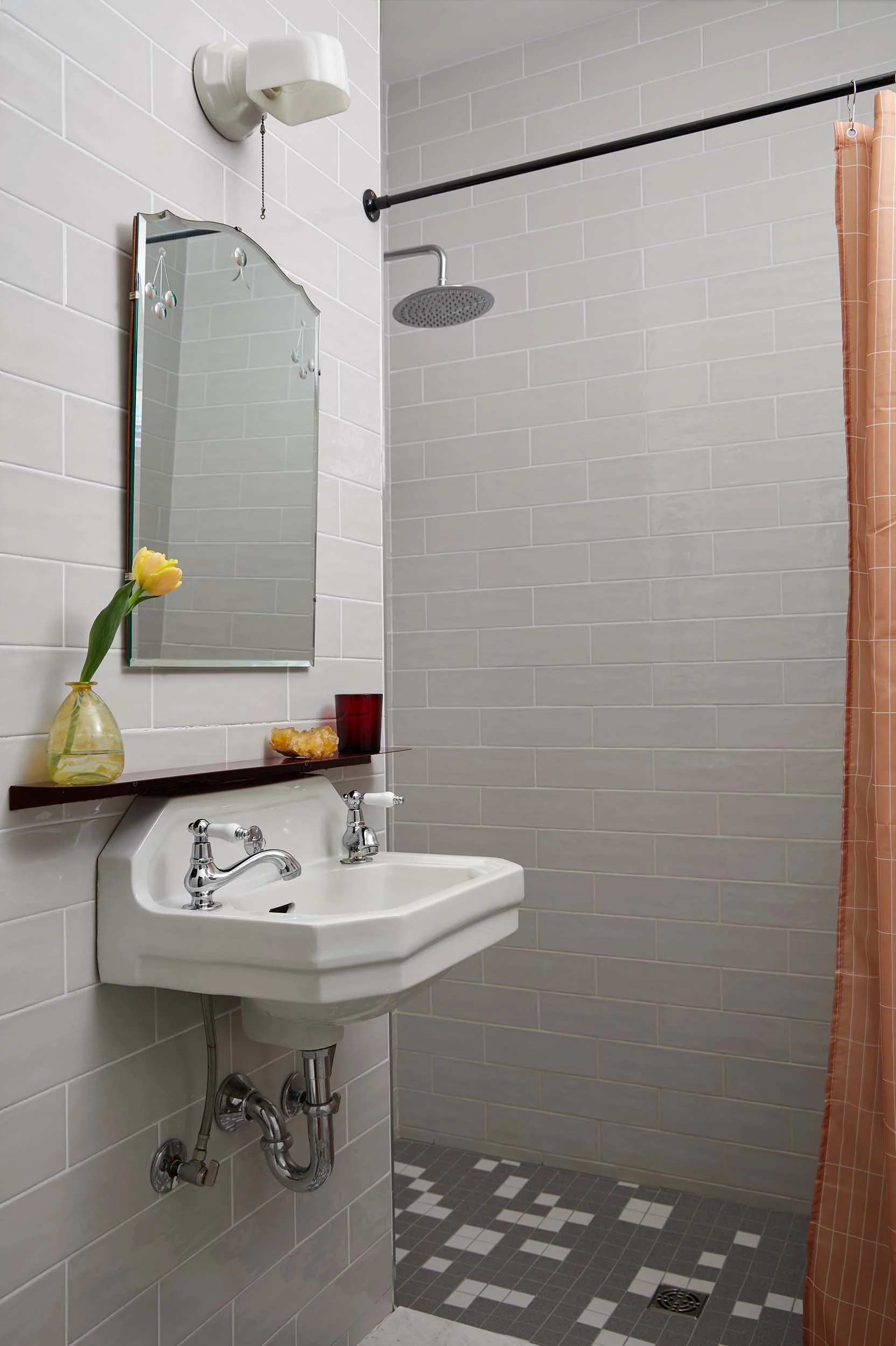 Small bathroom with a wall-mounted sink, a mirror, a showerhead, a shower curtain, and decorative tiles on the wall and floor.