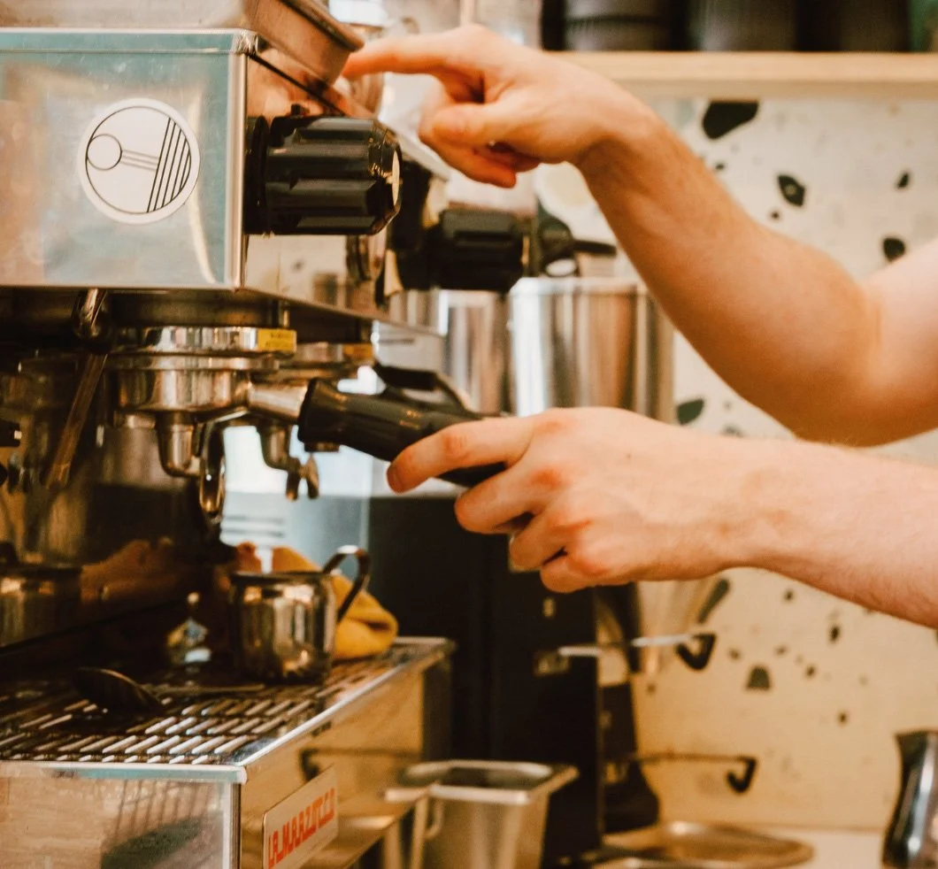 Person opens and adjusts a commercial espresso machine in a coffee shop.