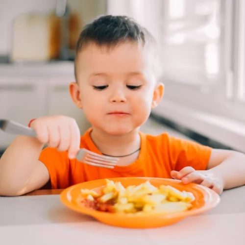 Un jeune garçon mange des pâtes dans une assiette orange
