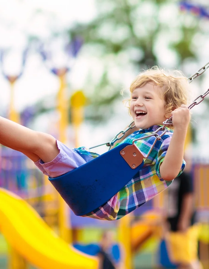 Un enfant souriant qui joue sur une balançoire dans un parc d'attractions.