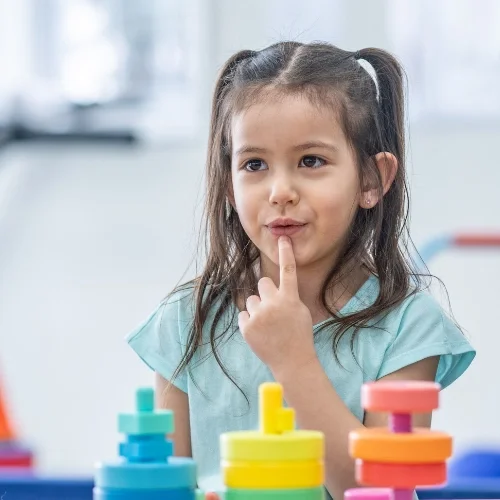 Une jeune fille avec des cheveux en queue de cheval réfléchissant, entourée de jeux de construction colorés.