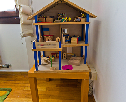 Una casetta dei giochi in legno su un tavolo, con soffitto a tetto e pareti colorate blu e beige, piena di vari giocattoli