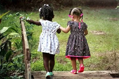 Due bambine che camminano insieme su un sentiero di prato, tenendosi per mano in un ambiente naturale.