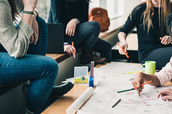 Gruppo di persone che lavora o si riunisce intorno a un grande foglio di carta con appunti e disegni.