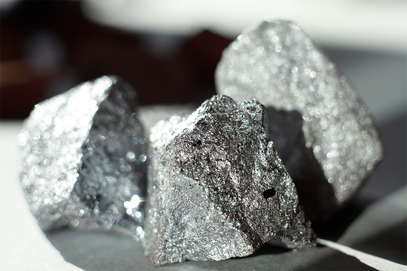 Three metallic gray rocks with shiny, reflective surfaces sit on a gray surface.