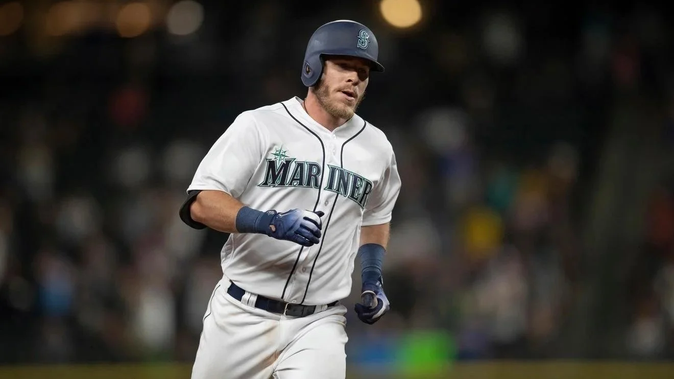 A baseball player in a Seattle Mariners uniform running on the field during a game, wearing a batting helmet and blue gloves.